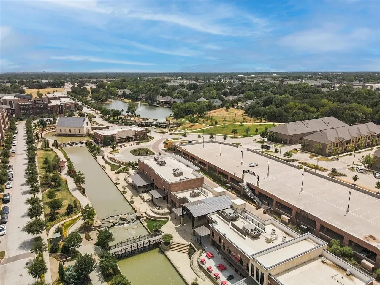 Aerial perspective showcasing a mixed-use development with a prominent waterway, multiple commercial buildings, structured parking facilities, and surrounding green spaces