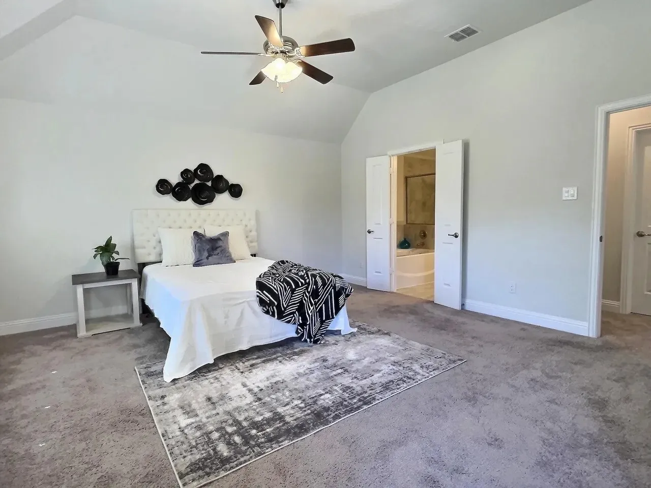 Vaulted ceiling, ceiling fan, carpet flooring, double doors, and an en-suite bathroom with a built-in tub