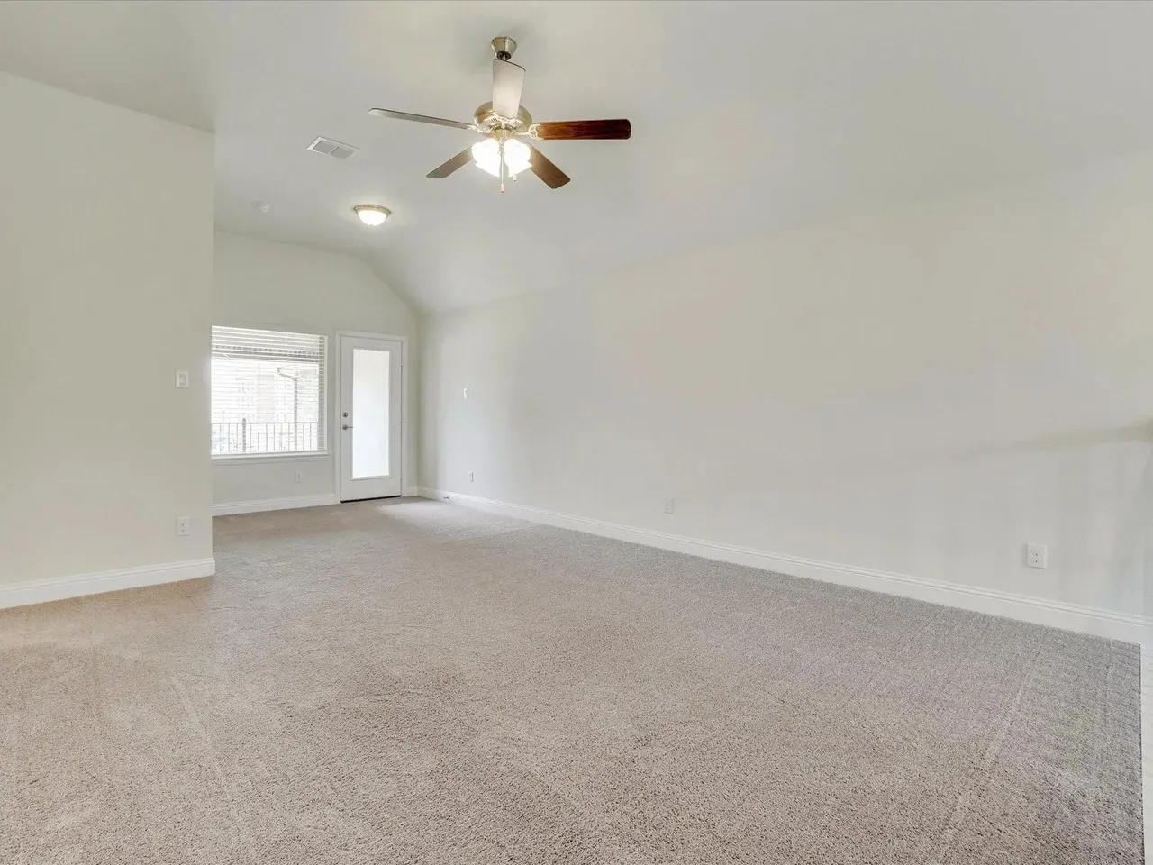 Spacious room with vaulted ceiling, neutral carpeting, and a ceiling fan with integrated lighting