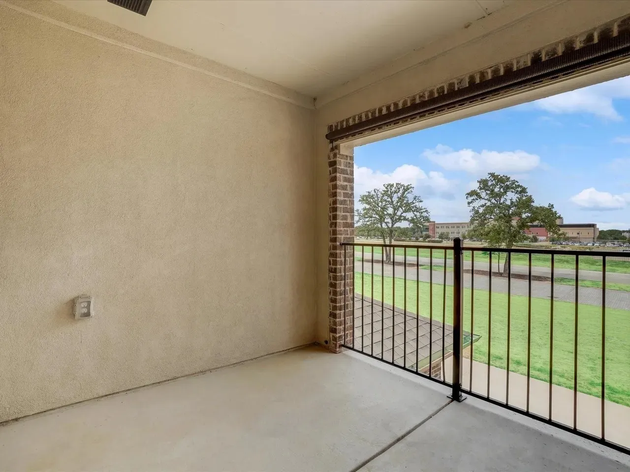 Covered balcony with a concrete floor, textured wall finish, and a black metal railing
