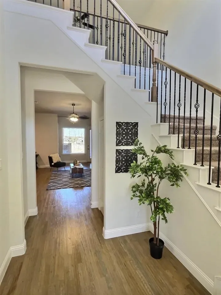 Wood-finish flooring throughout, staircase with carpeted treads, wrought iron balusters, and wood handrail, white baseboards