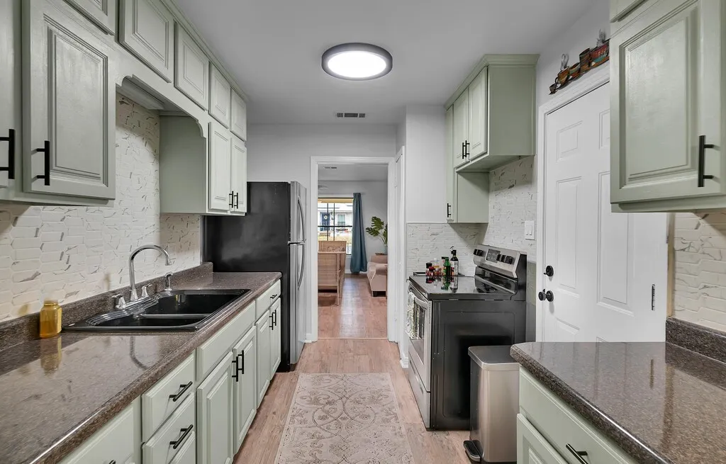 Galley kitchen featuring light-toned cabinetry, dark countertops, a double basin sink, and a black appliance suite