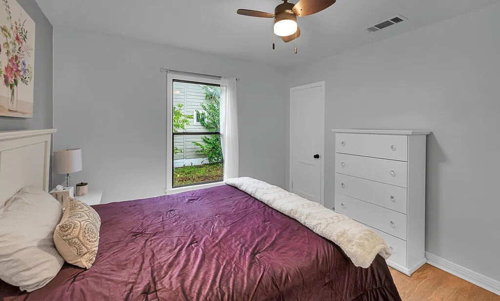 Wood-finish flooring, ceiling fan with integrated lighting, white paneled door, and a single window