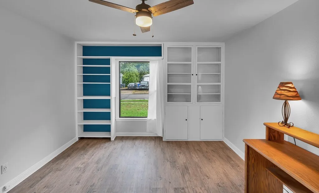 Wood-finish flooring, built-in shelving, built-in cabinetry with glass inserts, and a ceiling fan with integrated lighting