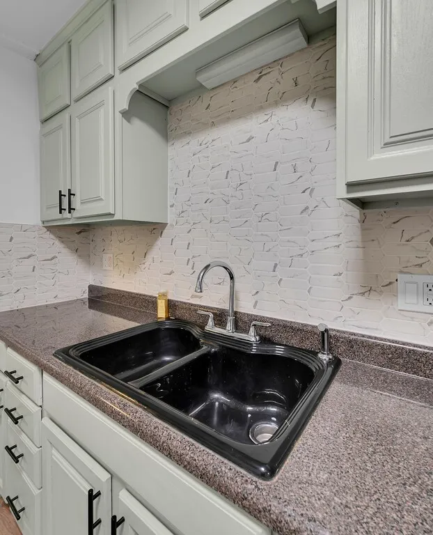 Light-toned cabinetry with modern black hardware, dual basin sink, chrome faucet, and textured tile backsplash