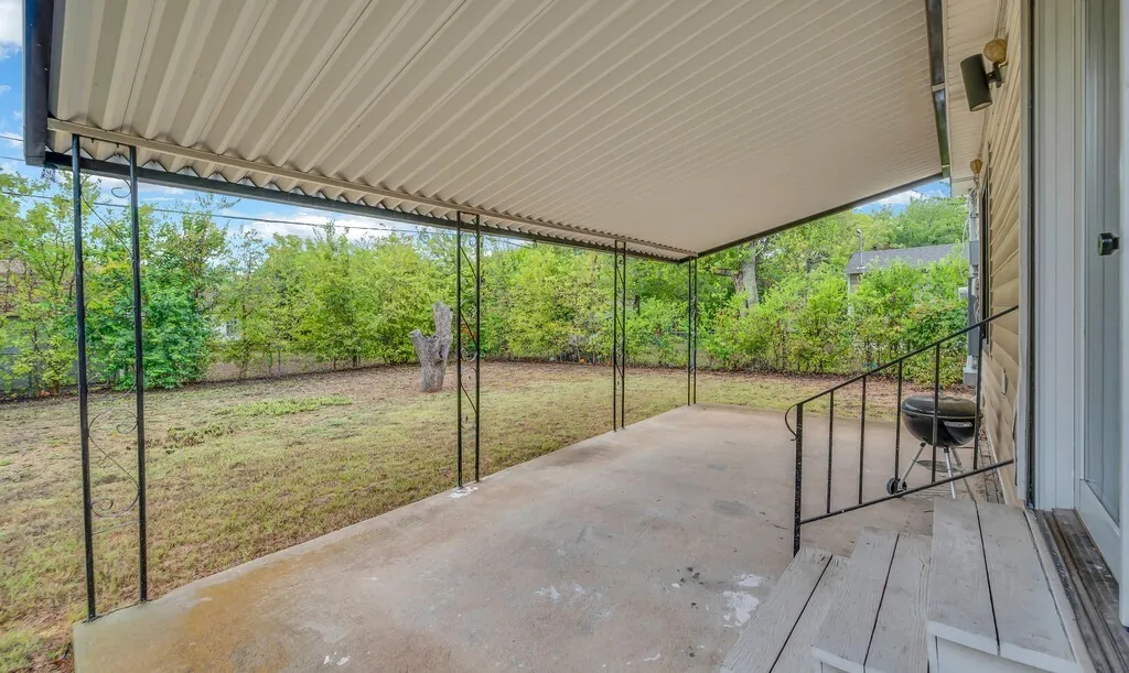 Covered concrete patio with metal support posts, wood-finish steps, and a metal handrail