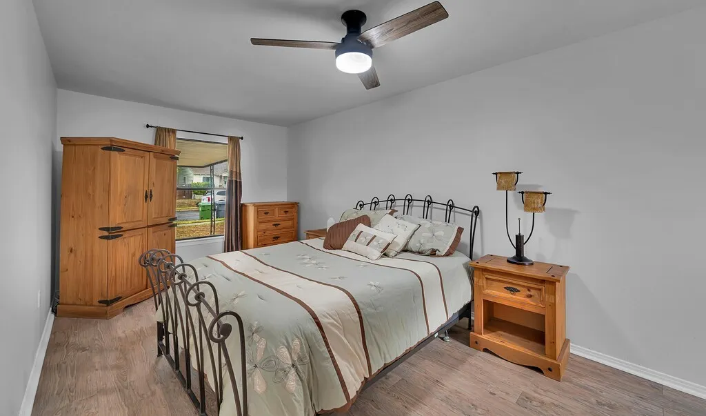 Wood-finish flooring, a window with curtains, and a ceiling fan with integrated lighting