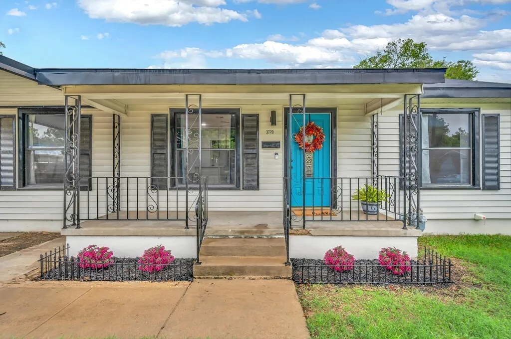 Covered front porch with decorative wrought iron railings, white siding, black shutters, and a vibrant blue entry door