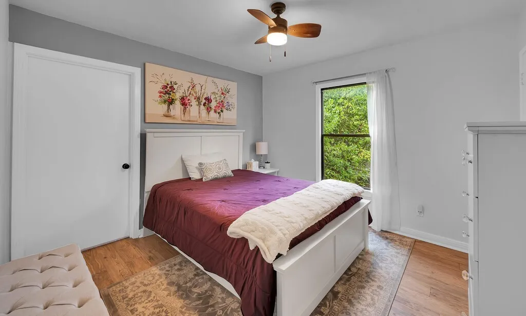 Bright secondary bedroom with gray walls, wood-finish flooring, and natural light from a large window