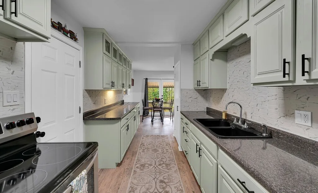 Kitchen featuring wood-finish flooring, light green cabinetry with black hardware, dark countertops, and a white tiled backsplash