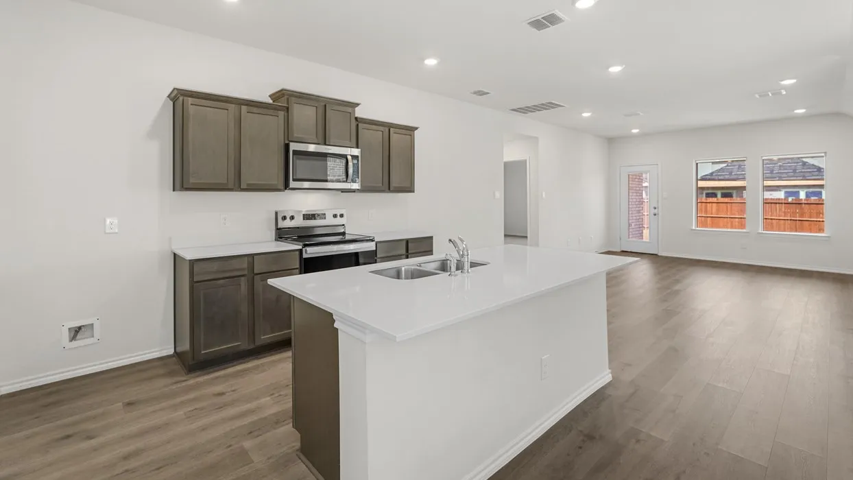 Open concept kitchen featuring an island with an integrated sink, white countertops, dark wood-finish cabinetry, stainless steel appliances, and recessed lighting