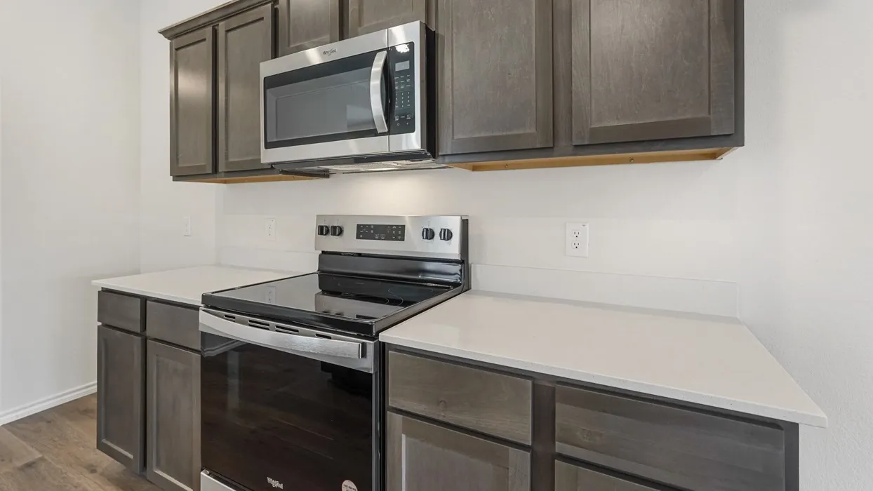 Modern kitchen featuring dark wood-finish cabinetry, light countertops, and a stainless steel range with an overhead microwave
