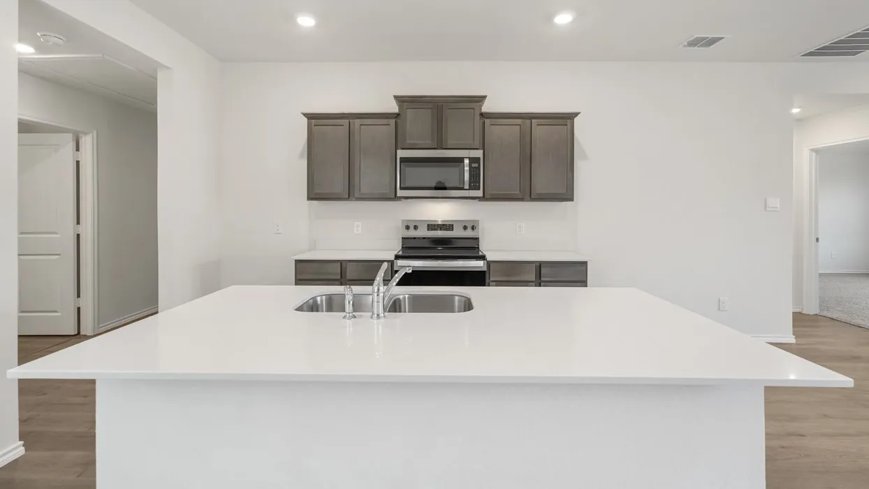 Kitchen featuring an expansive island with a double basin stainless steel sink, light-colored countertops, wood-finish flooring, recessed lighting, and dark wood cabinetry with stainless steel appliances