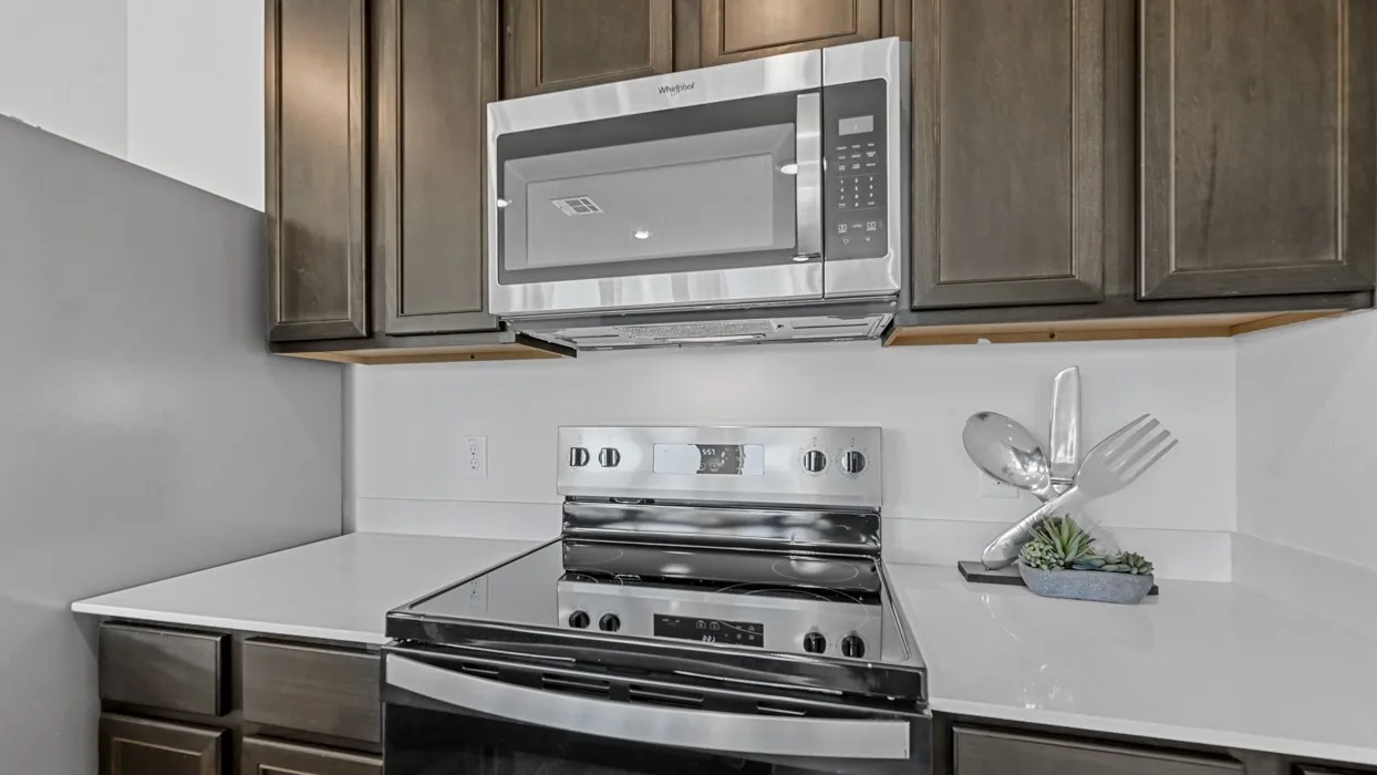Stainless steel range with a glass cooktop, stainless steel microwave, dark wood-finish cabinetry, and solid surface countertops
