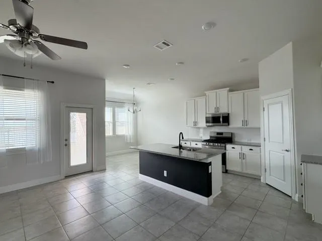 Open-concept kitchen and living area featuring tile flooring, white cabinetry, stainless steel appliances, a kitchen island with a dark base, and recessed lighting
