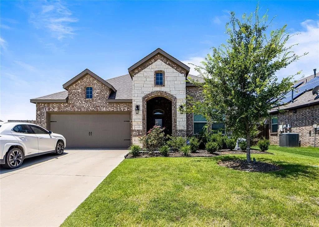 Brick and stone façade, arched entryway, attached garage, concrete driveway, and landscaped front yard