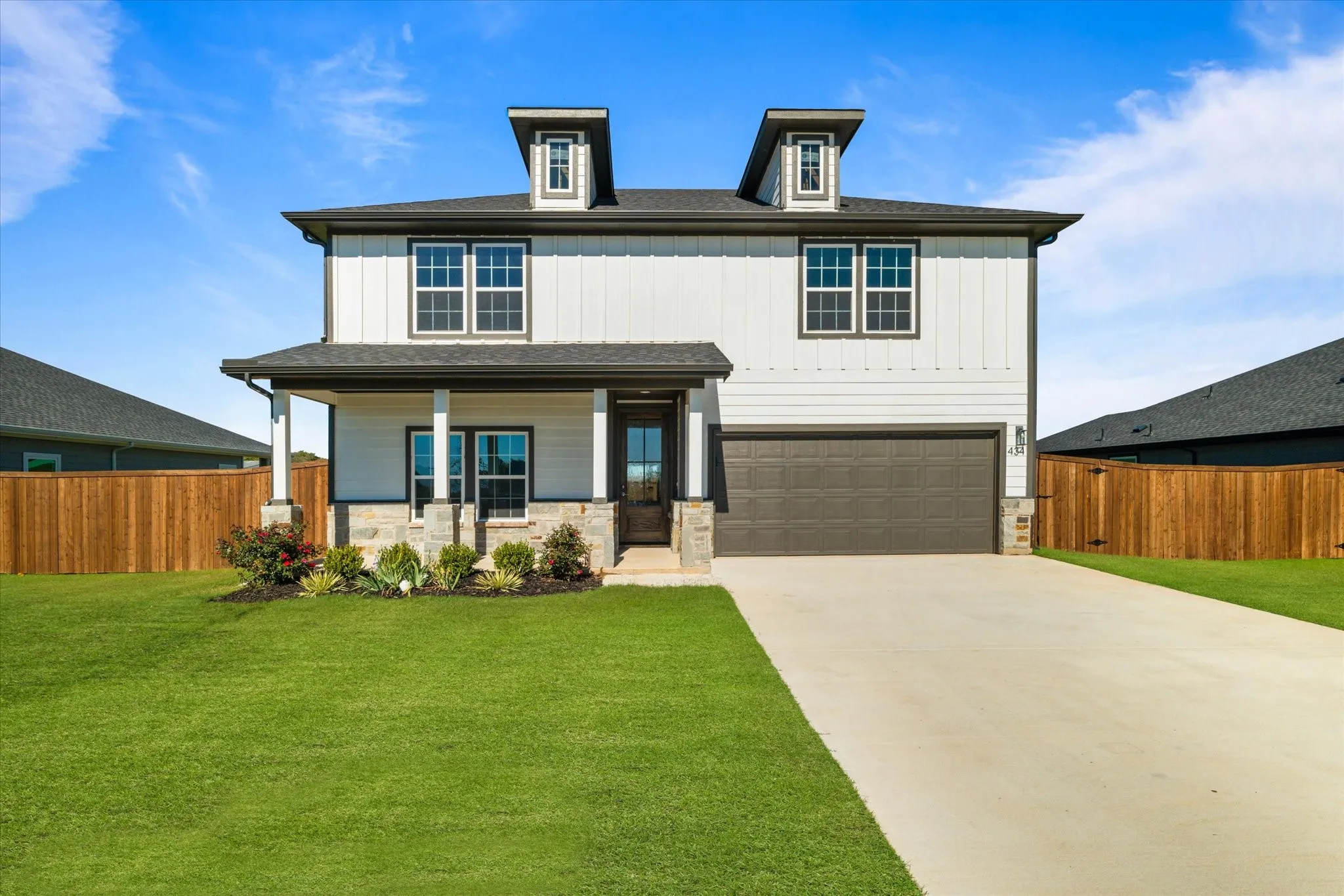 Two-story residence featuring a covered front porch with stone accents, a two-car garage, and a concrete driveway