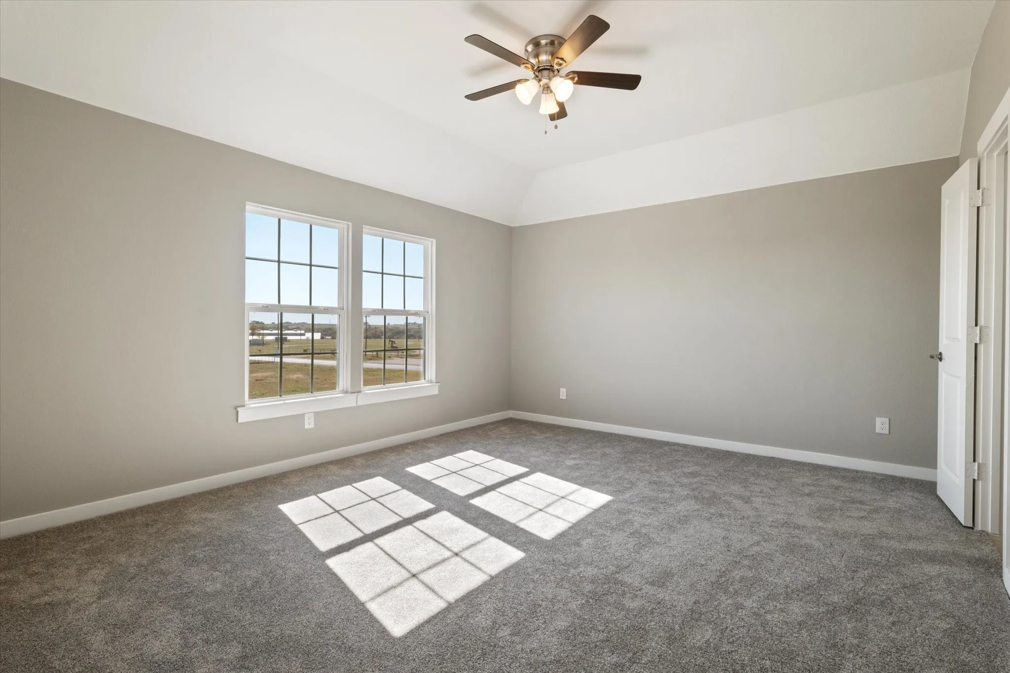 Two pane windows, neutral gray walls, gray carpeting, tray ceiling, and a ceiling fan