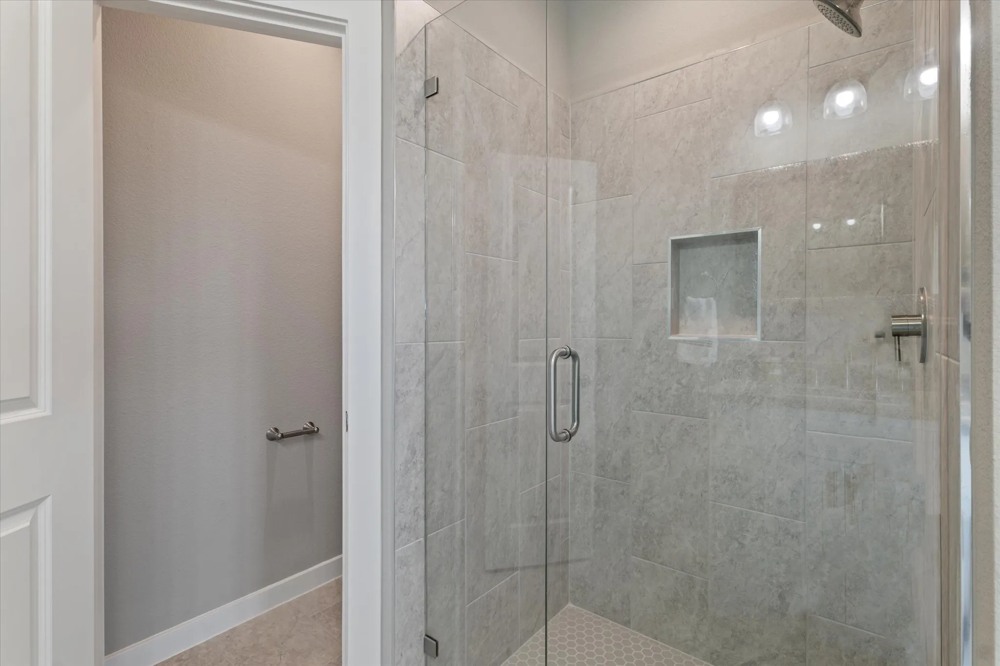 Glass-enclosed shower with a recessed shelf, tile surround, and hexagonal tile flooring