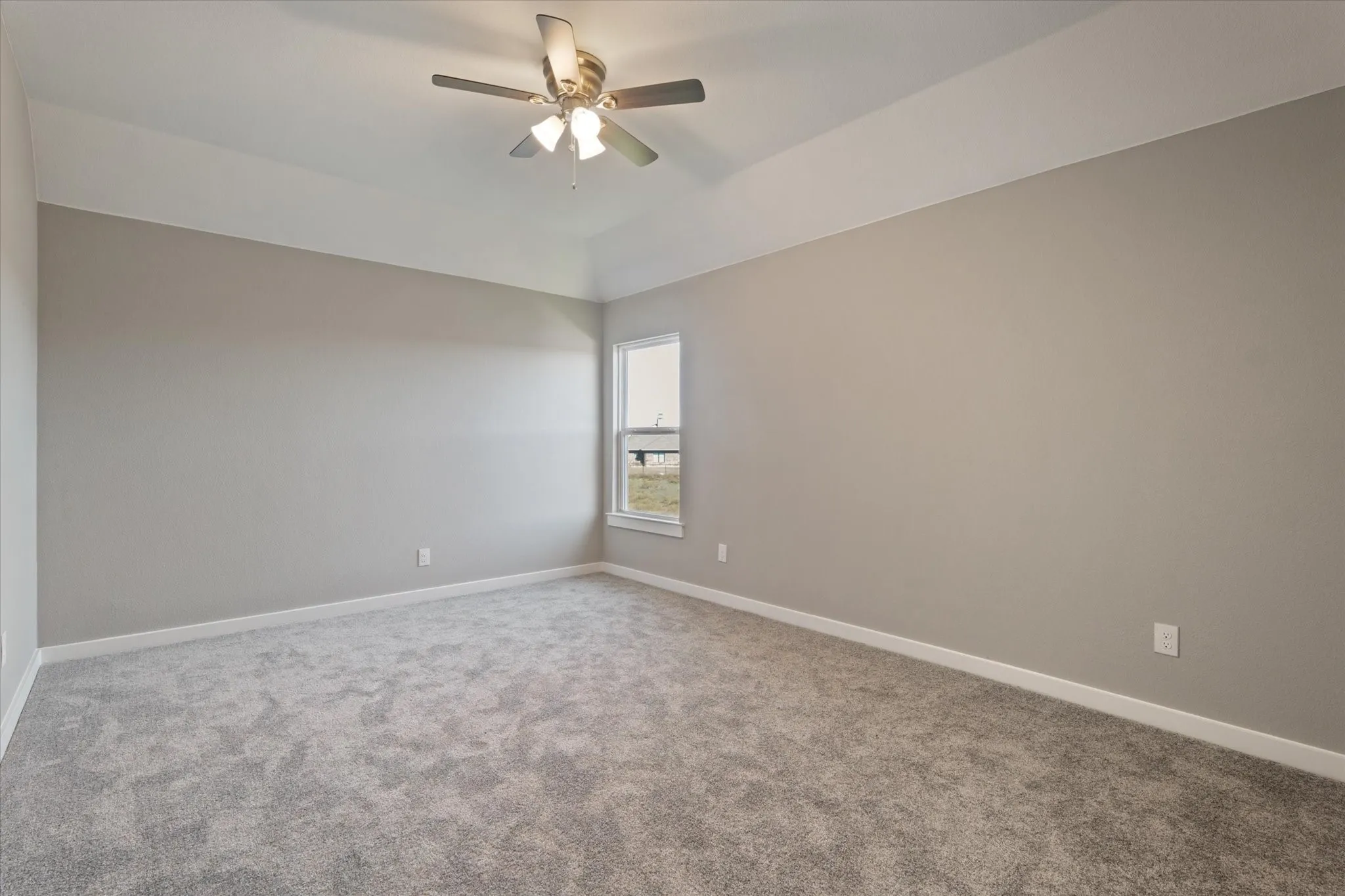 Tray ceiling, ceiling fan with integrated lighting, window with white trim, light gray carpet flooring, and neutral wall paint