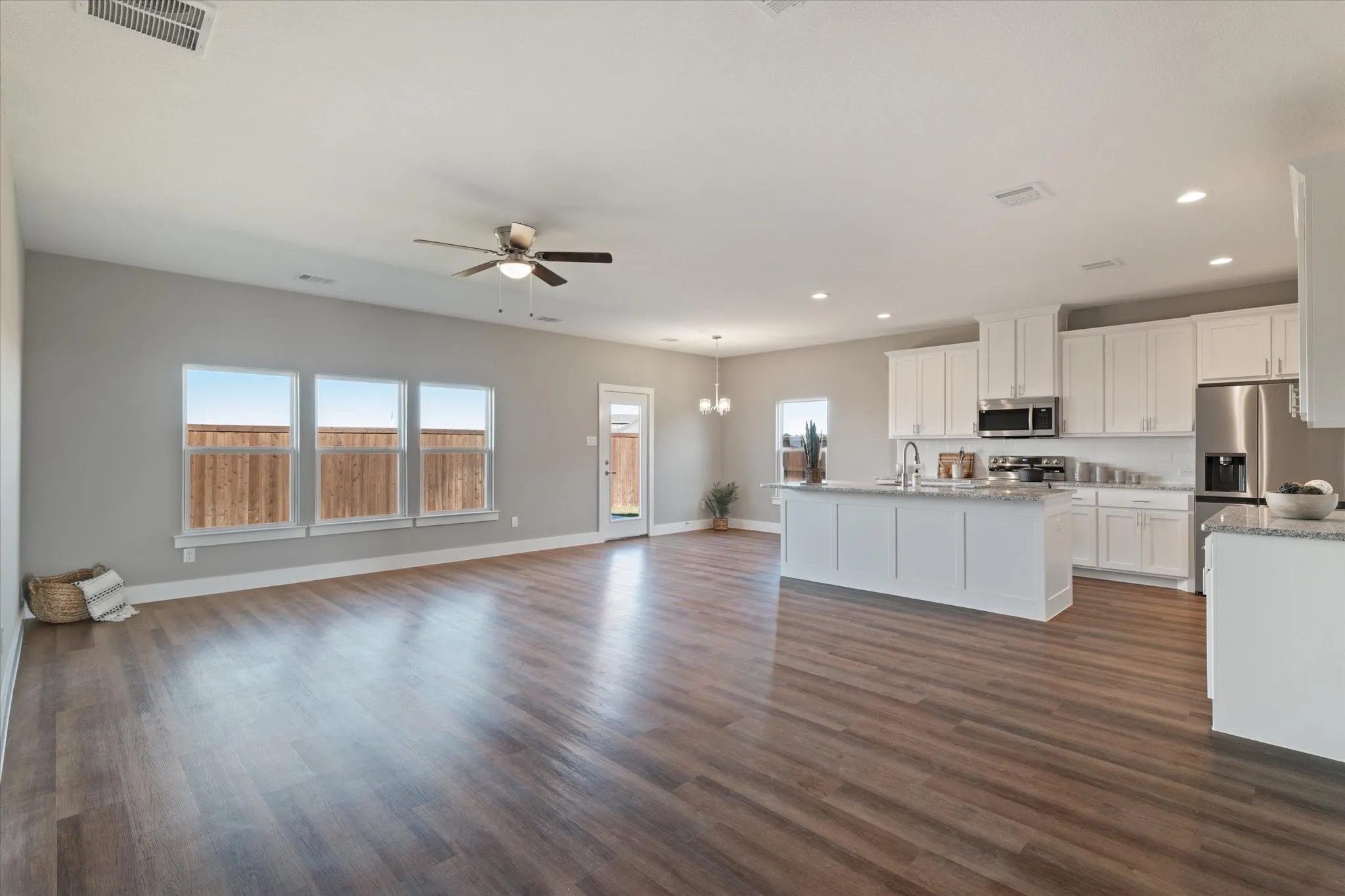 Open-concept living area with wood-finish flooring, white cabinetry, stainless steel appliances, and a kitchen island with a​​‌​​​​‌​​‌‌​‌‌​​​‌‌​‌​‌​‌​​​‌​​ sink
