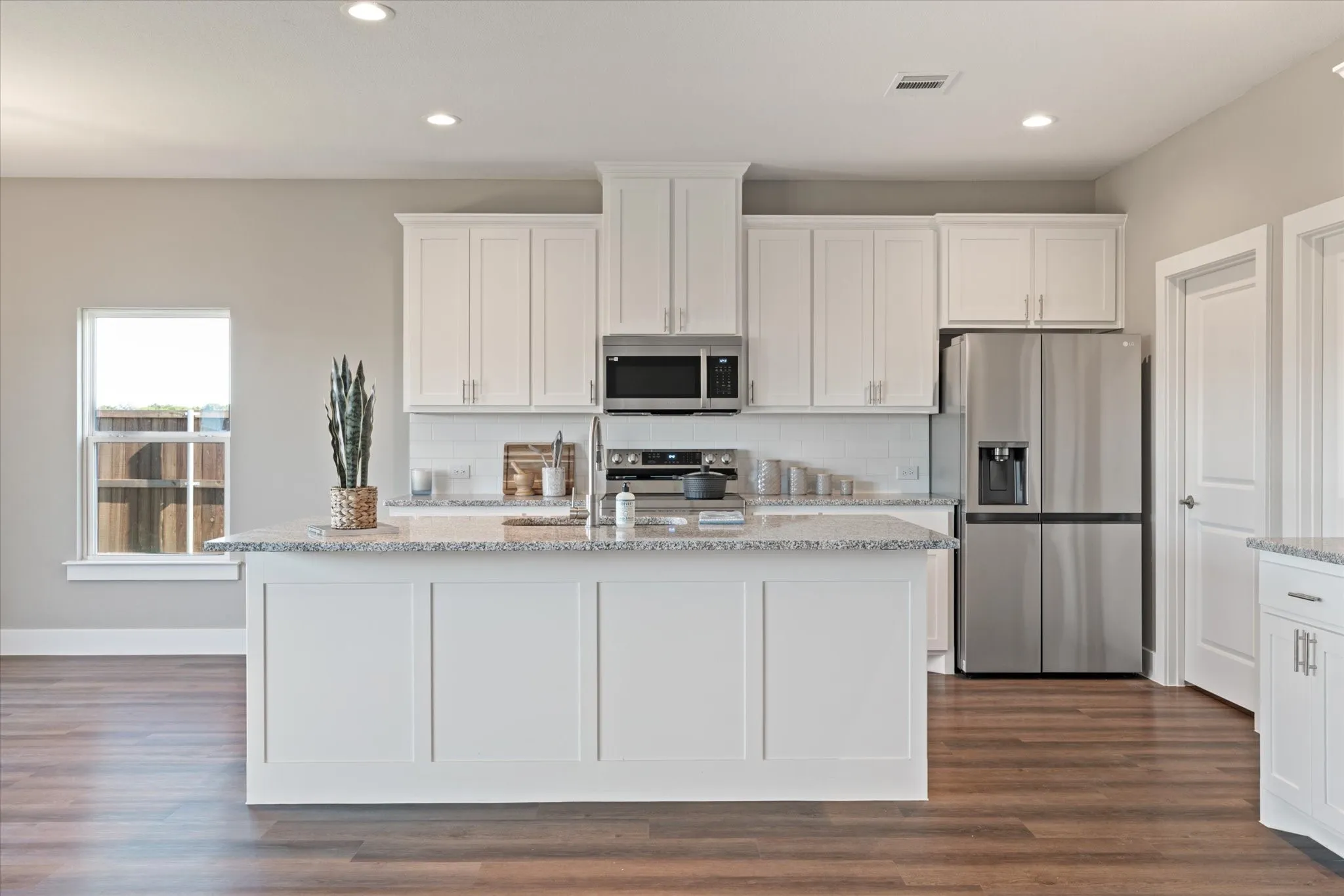 Kitchen featuring a central island with a light-toned countertop, white cabinetry, integrated stainless steel appliances, a tile backsplash, and recessed lighting