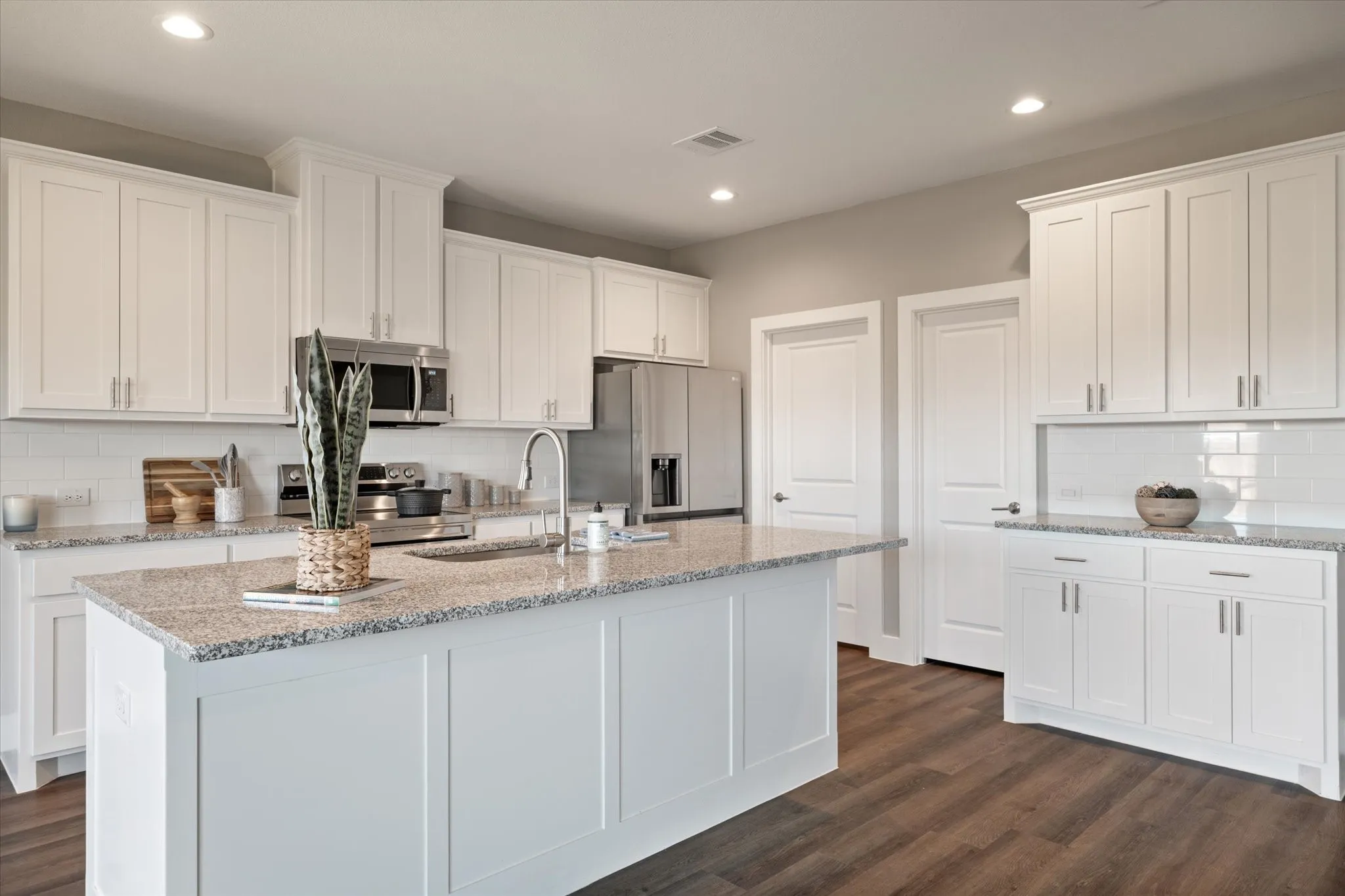 White shaker-style cabinetry, stainless steel appliances, granite countertops, subway tile backsplash, and wood-finish flooring