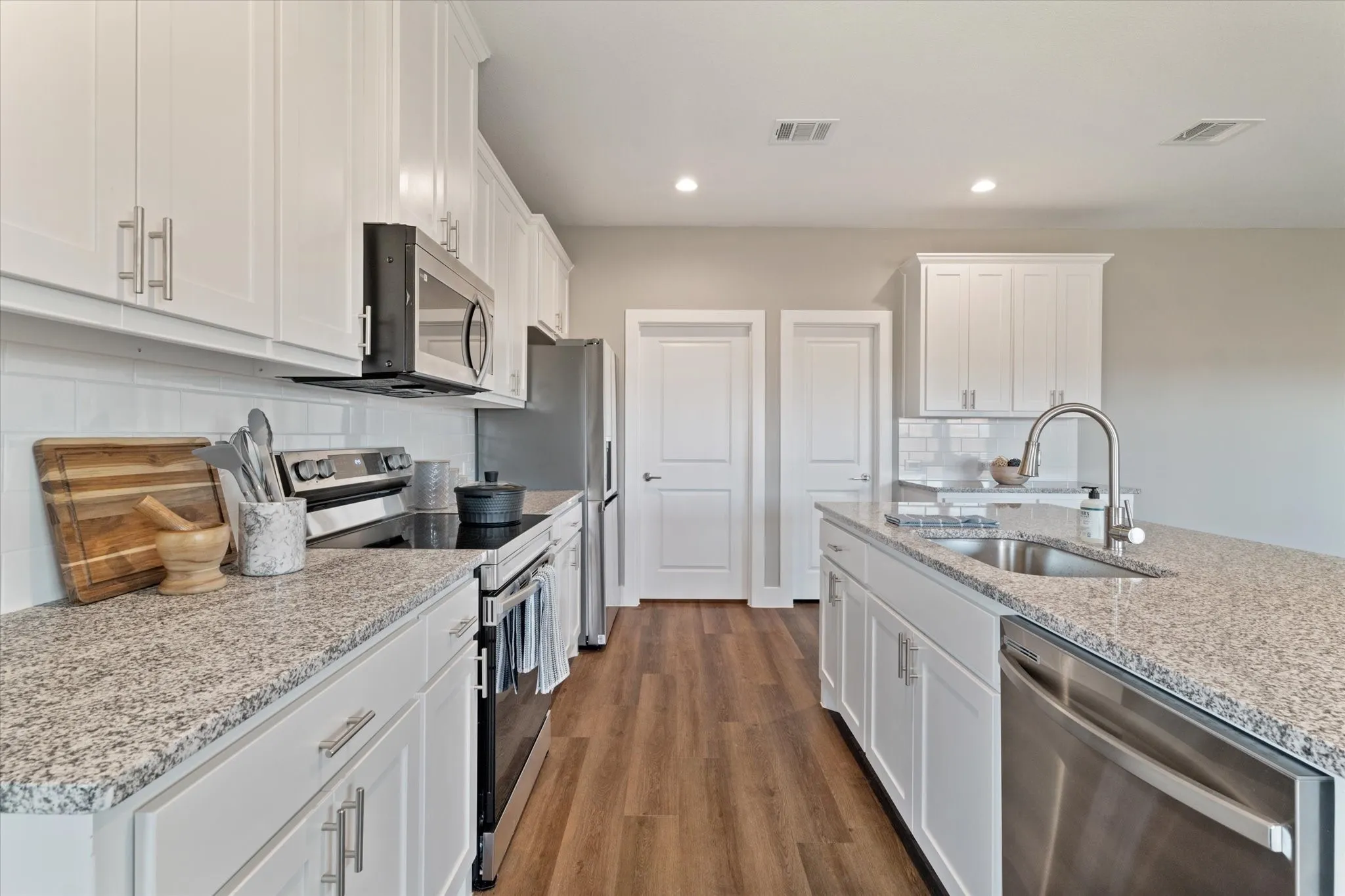 Kitchen featuring white cabinetry, gray speckled countertops, stainless steel appliances, wood-finish flooring, and a white subway tile backsplash