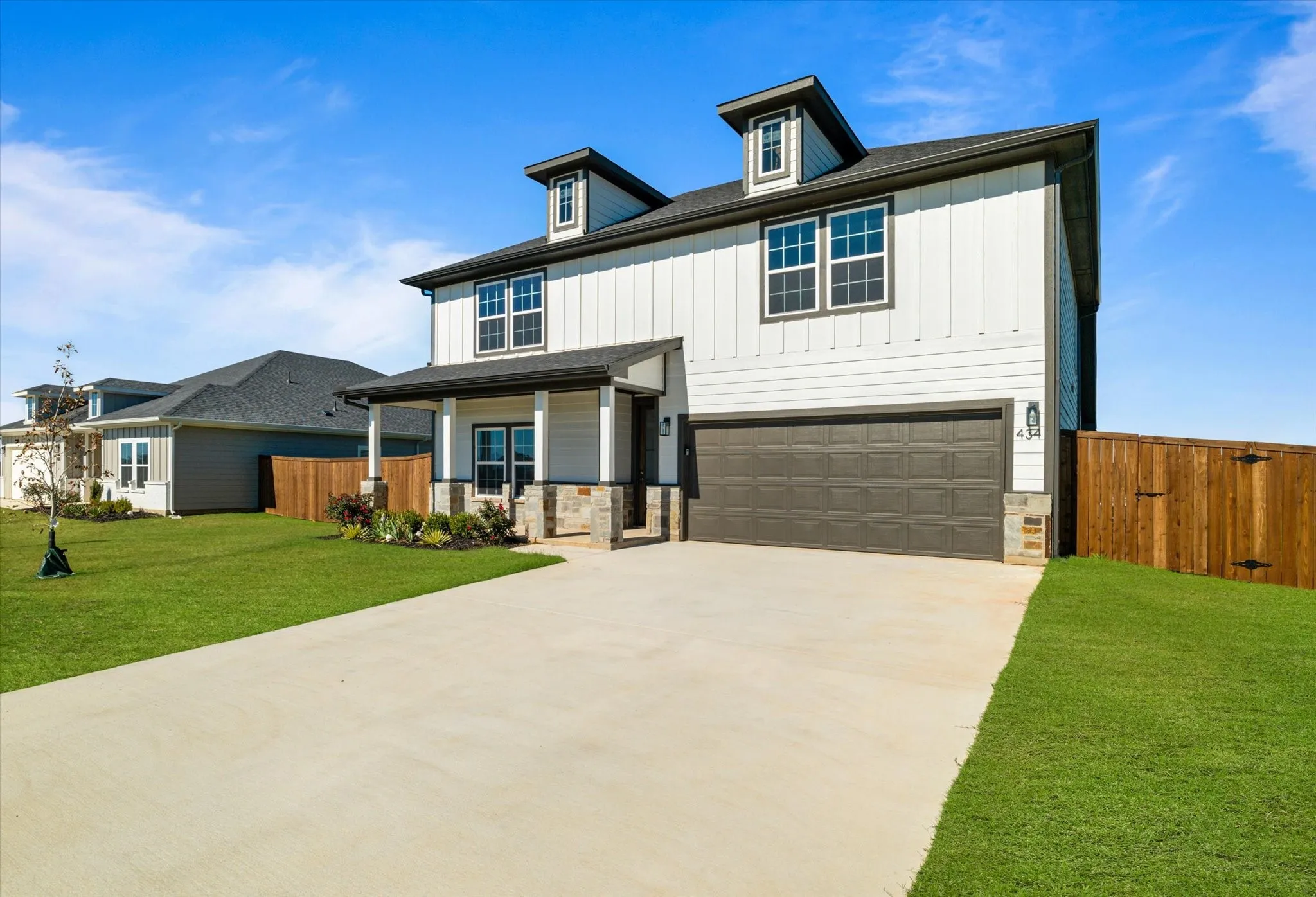 Two-story exterior with dormer windows, covered front porch, stone column accents, and an attached two-car garage