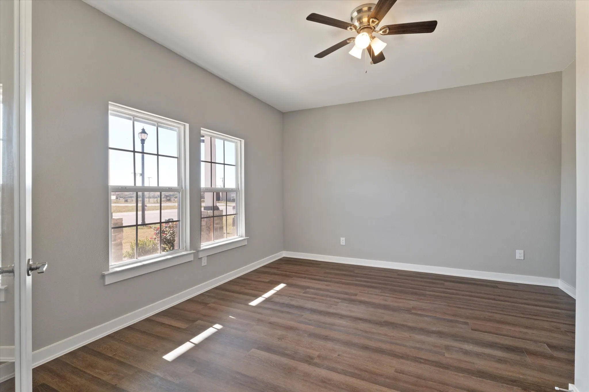 Wood-finish flooring, dual windows with grid patterns, light gray wall finish, and a ceiling fan with integrated lighting