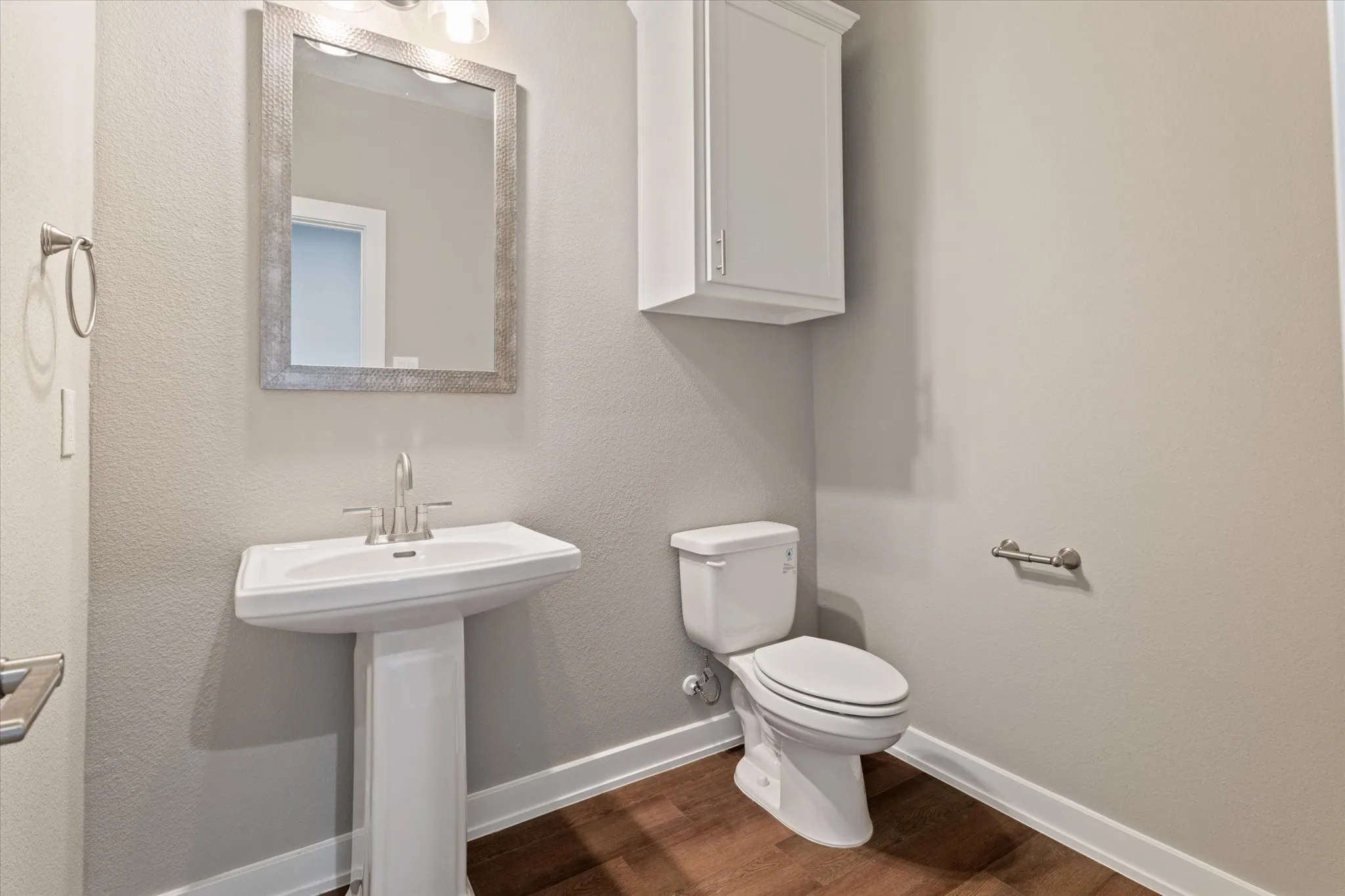 Pedestal sink with a polished chrome faucet, framed mirror, built-in upper cabinet, and wood-finish flooring