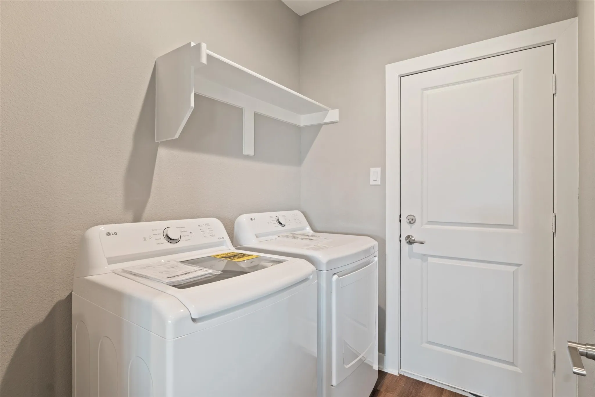 Laundry area featuring a wall-mounted shelf, light gray walls, and wood-finish flooring