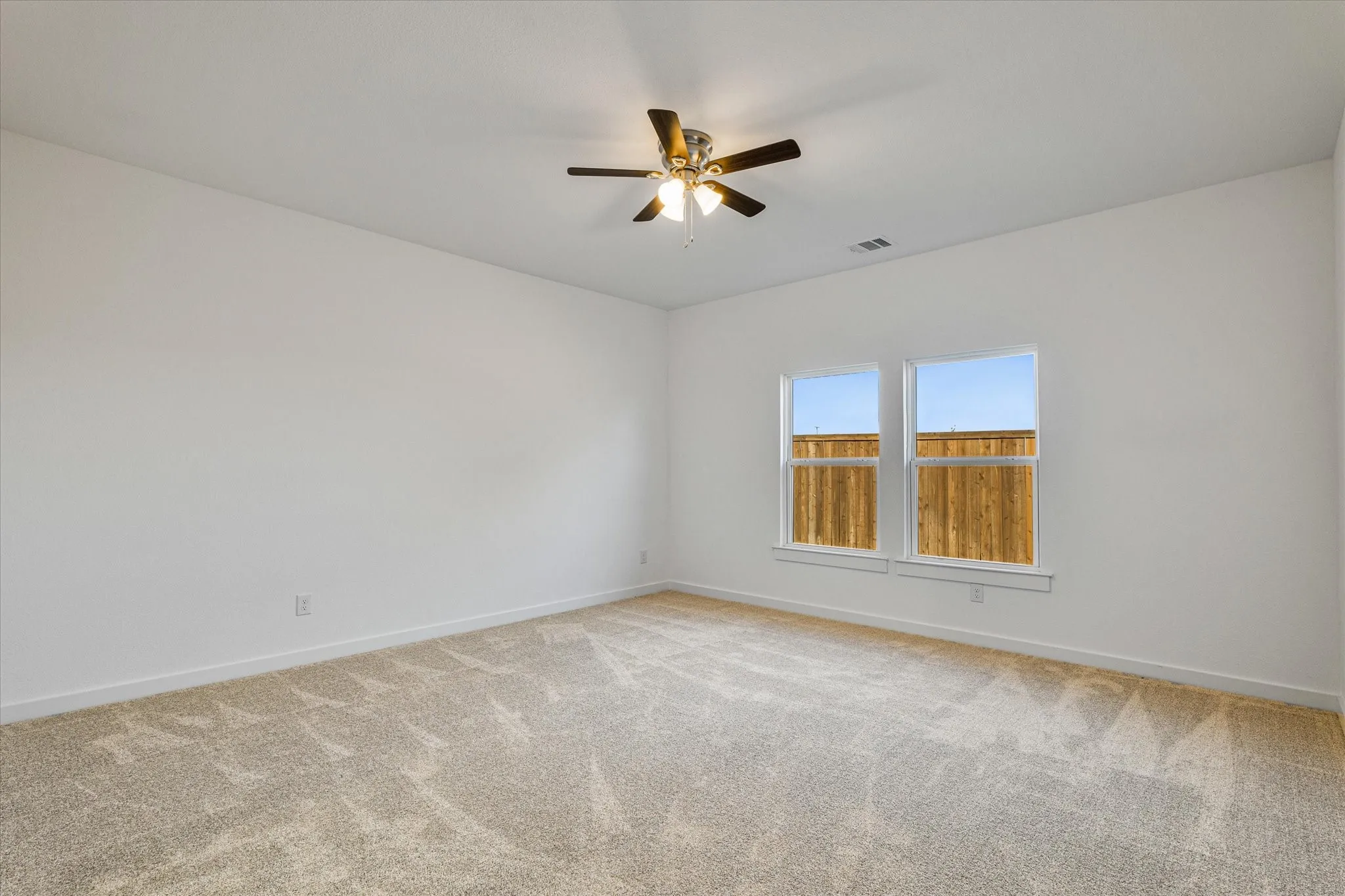 Two large windows, ceiling fan with integrated lighting, and neutral carpet flooring