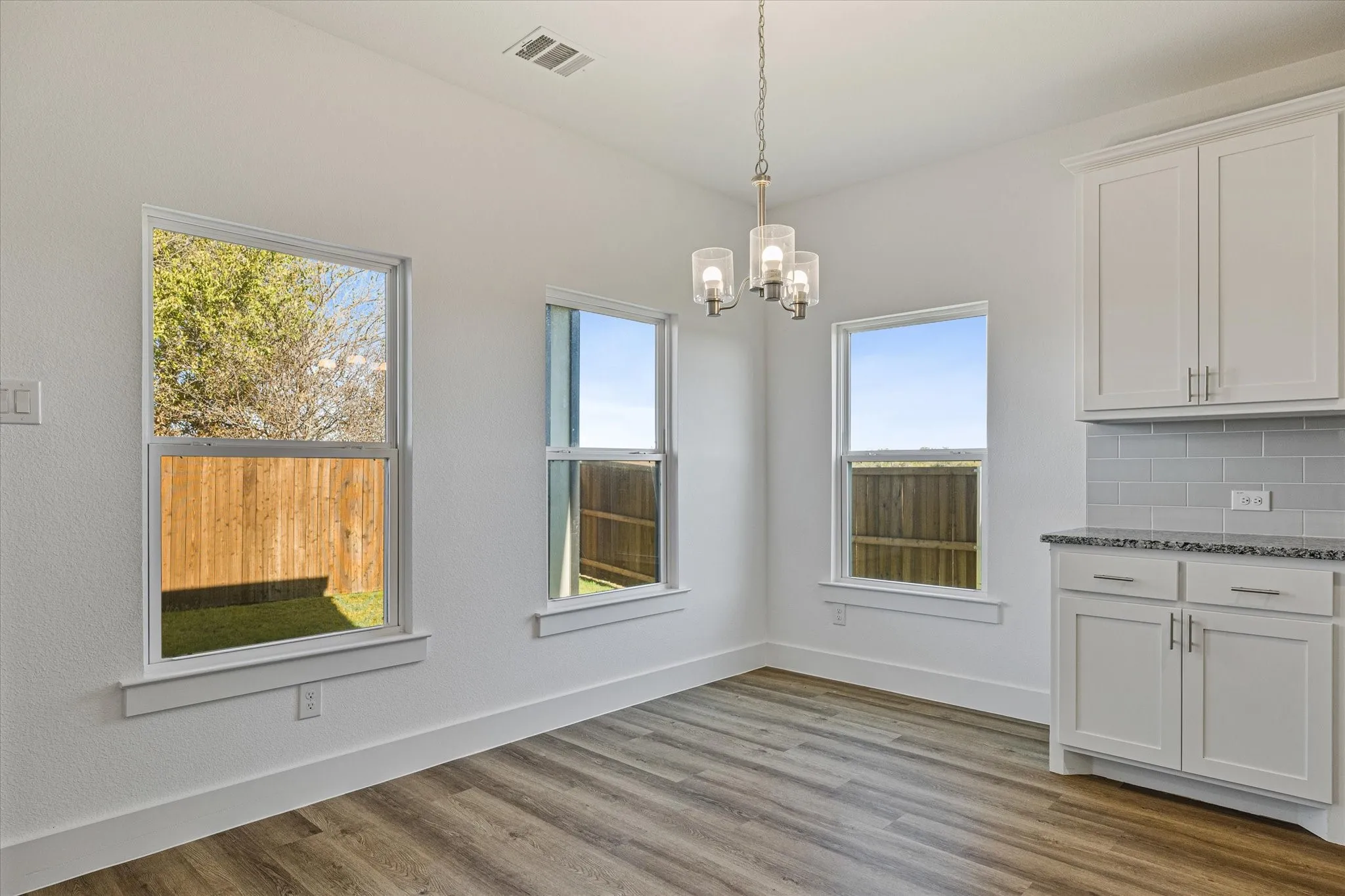 Wood-finish flooring with white baseboards, multiple windows, and a chandelier with glass shades
