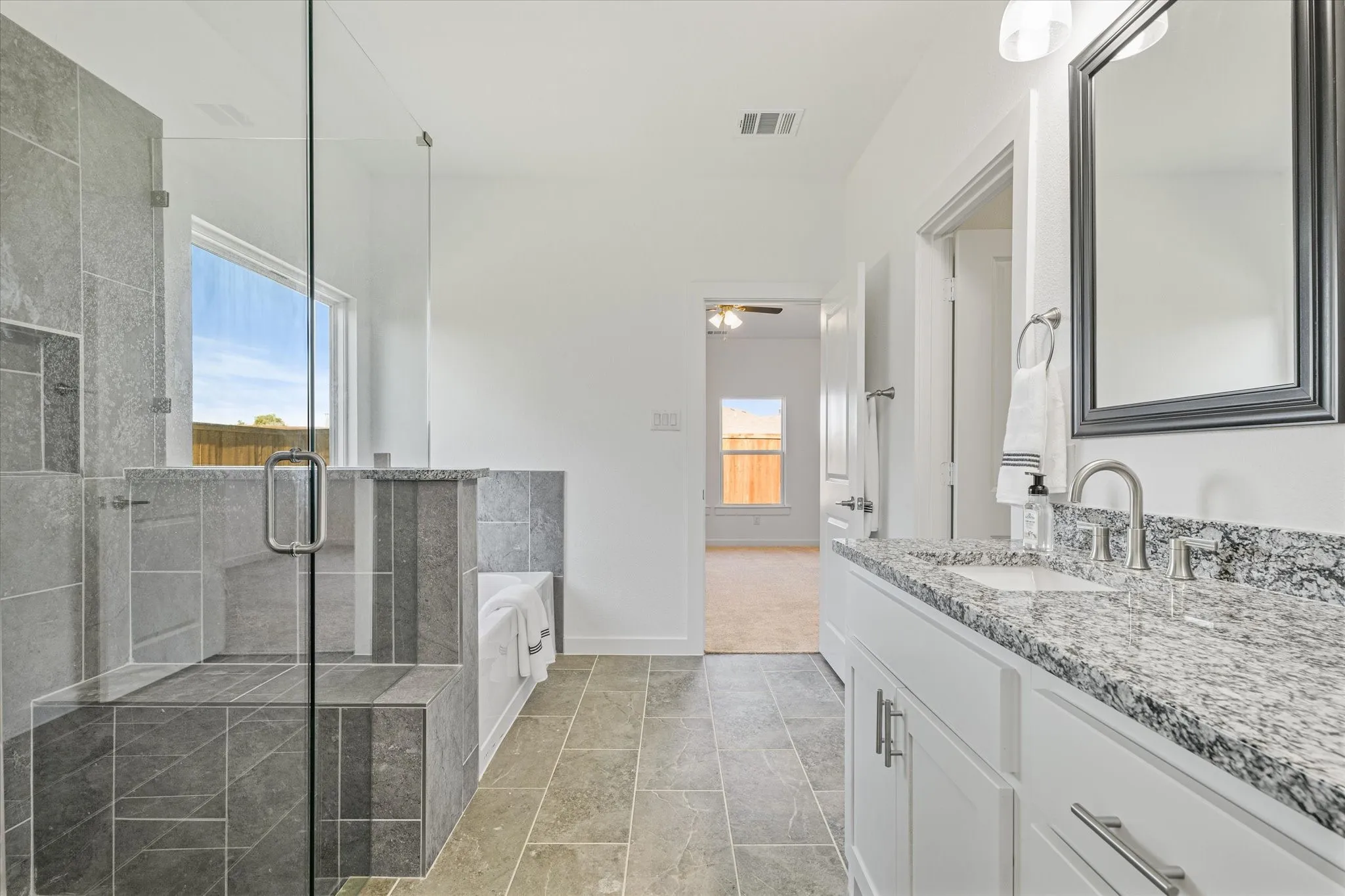 Spacious bathroom featuring a glass-enclosed shower with a built-in bench, a separate soaking tub, a dual vanity with a granite countertop, and tiled flooring