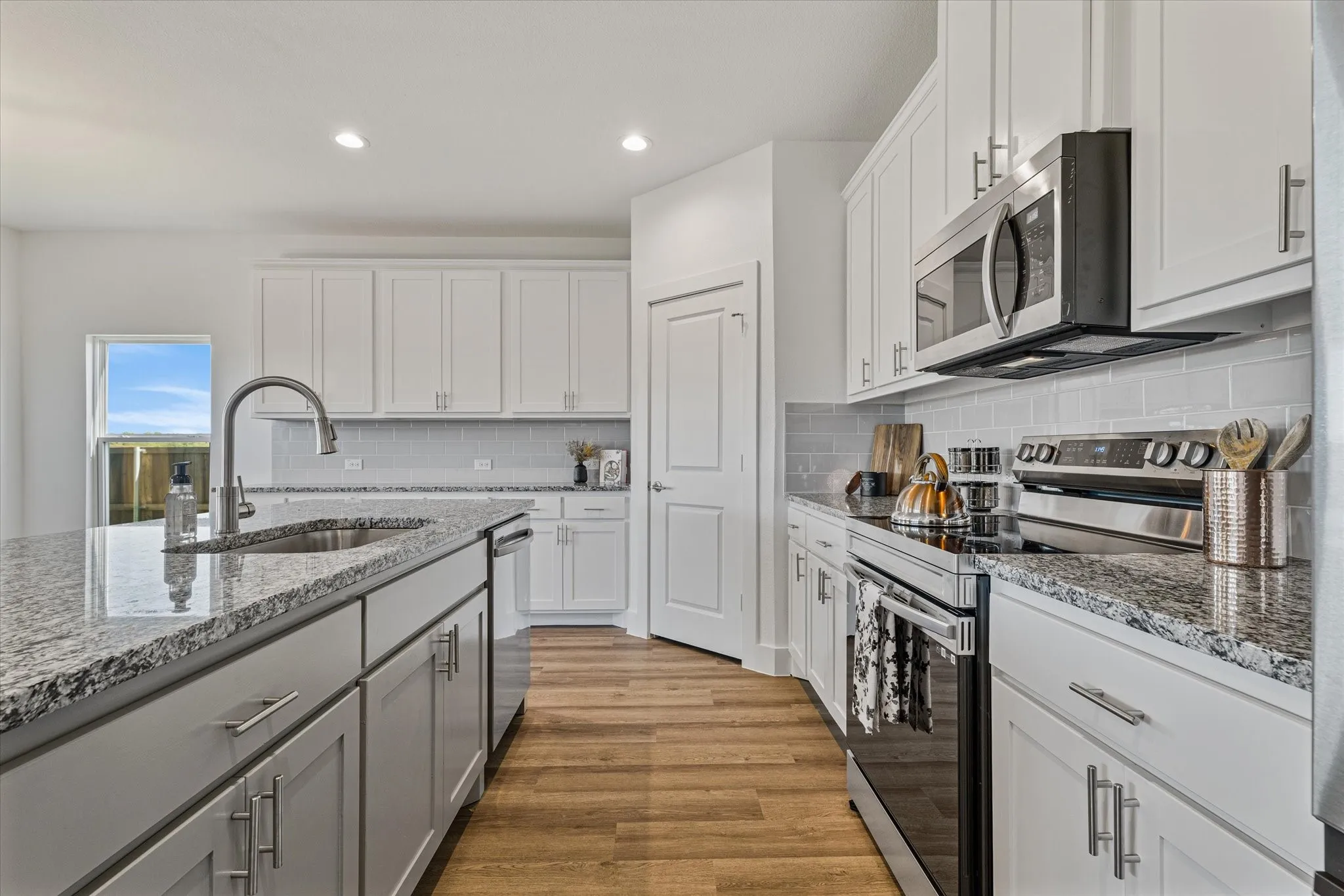 Kitchen featuring an island with an undermount sink, stainless steel appliances, granite countertops, white cabinetry, and wood-finish flooring