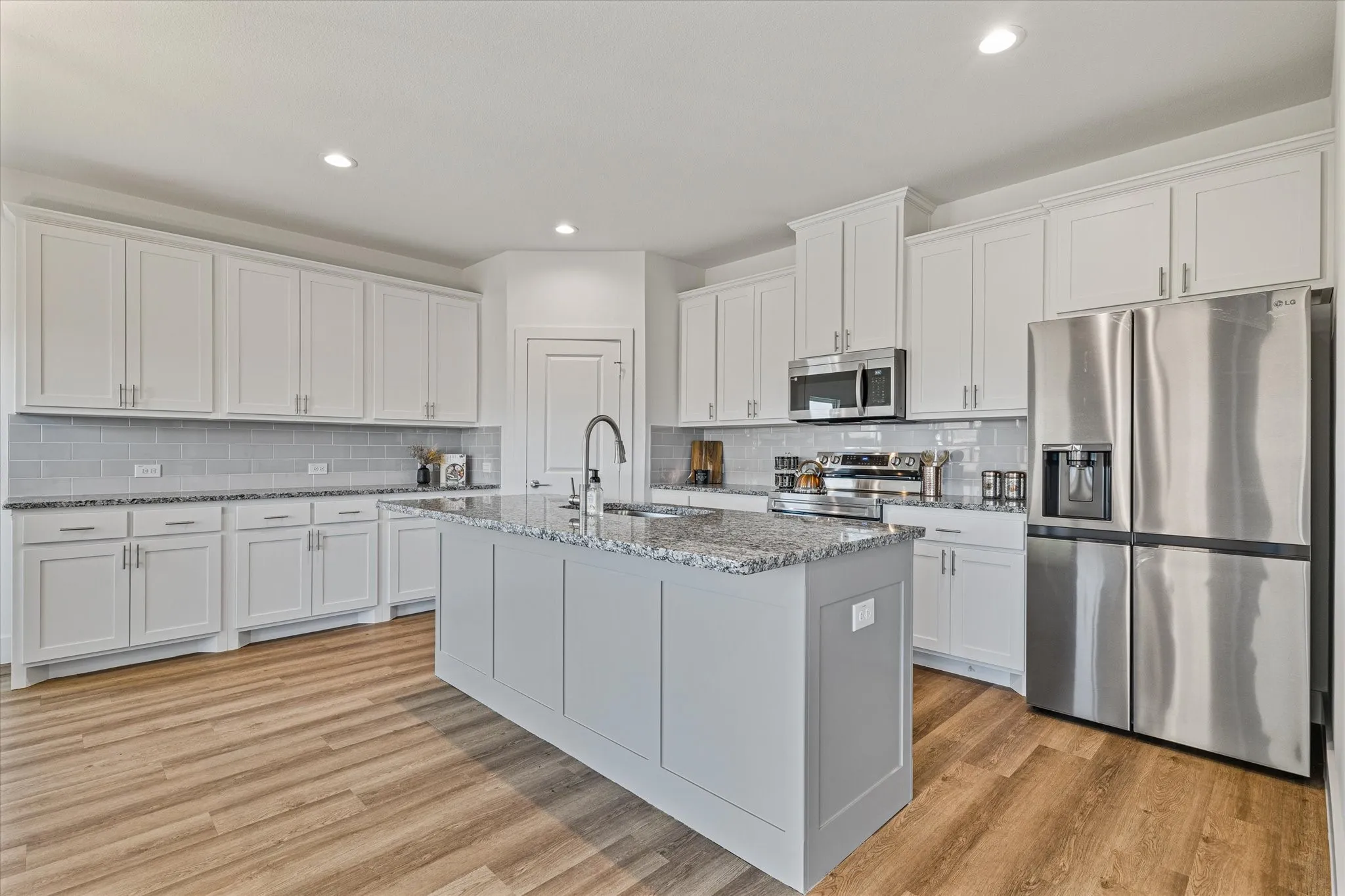 Kitchen featuring a large central island, full suite of stainless steel appliances, white shaker cabinetry, granite countertops, and a subway tile backsplash