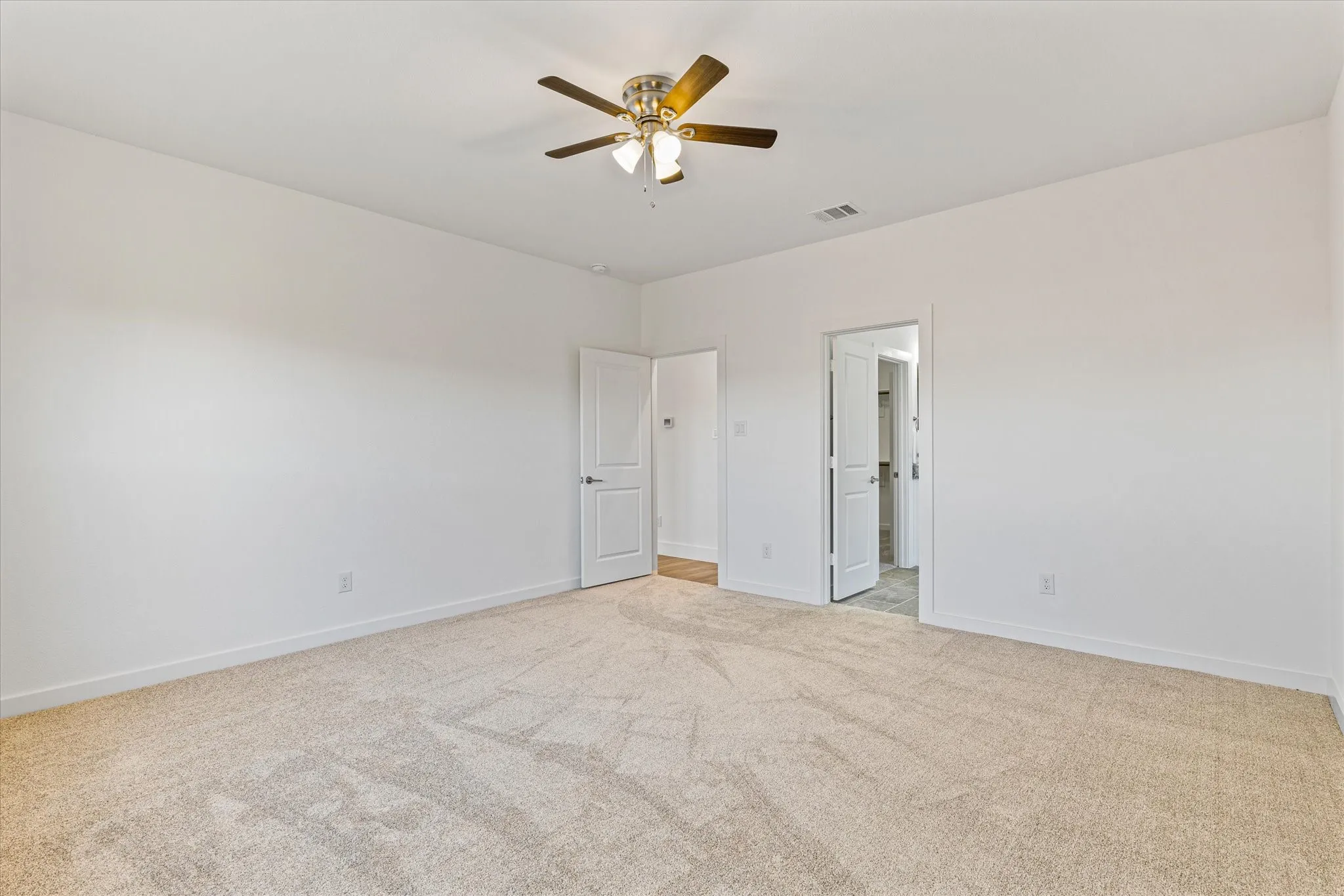 Spacious room featuring neutral carpeting, white walls, and a ceiling fan with integrated lighting