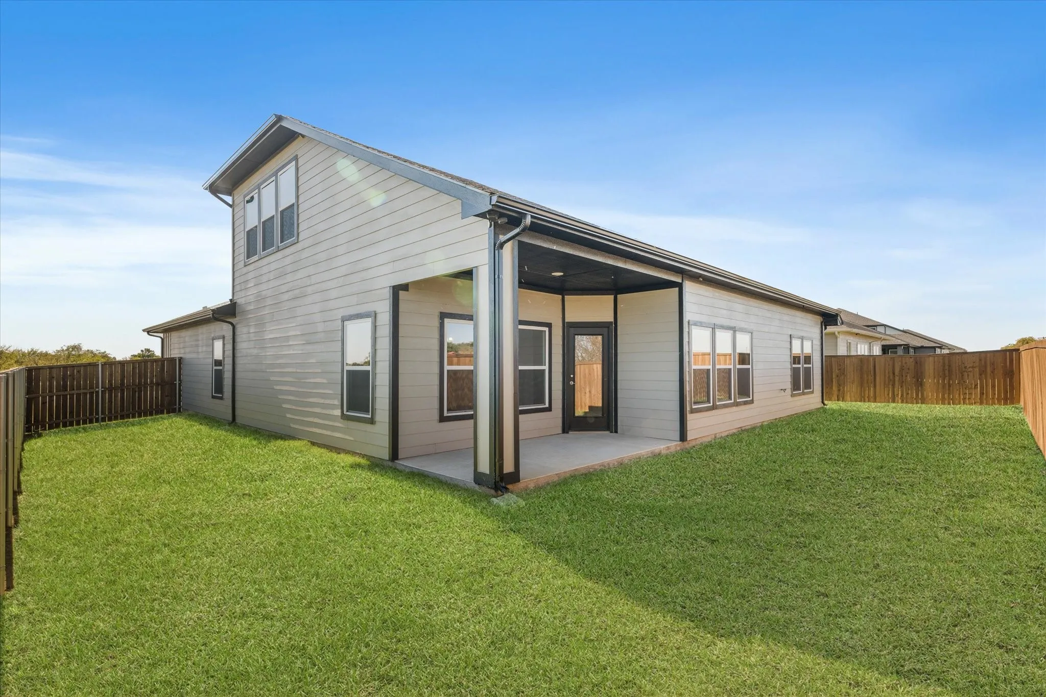 Expansive backyard featuring a covered patio, wood-tone fencing, and a manicured lawn