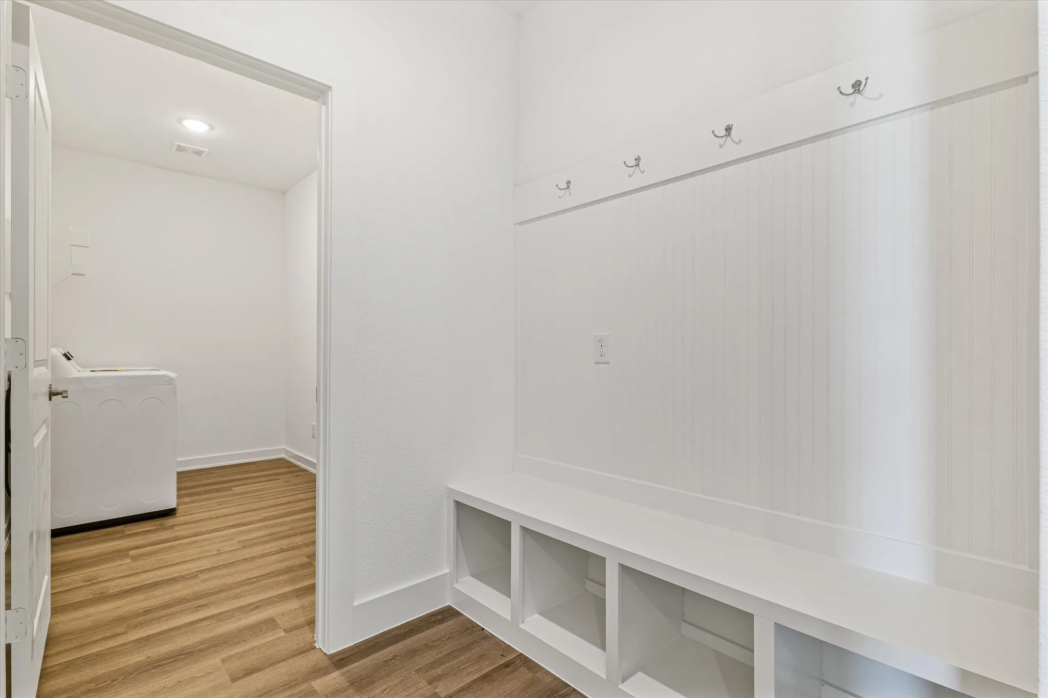 Built-in bench with storage cubbies, beadboard wall paneling, and wall-mounted coat hooks