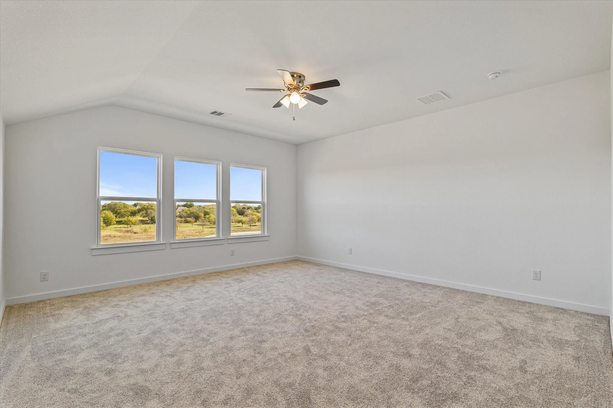 Vaulted ceiling with a contemporary ceiling fan, three large windows, neutral-toned carpeting, and light-colored walls