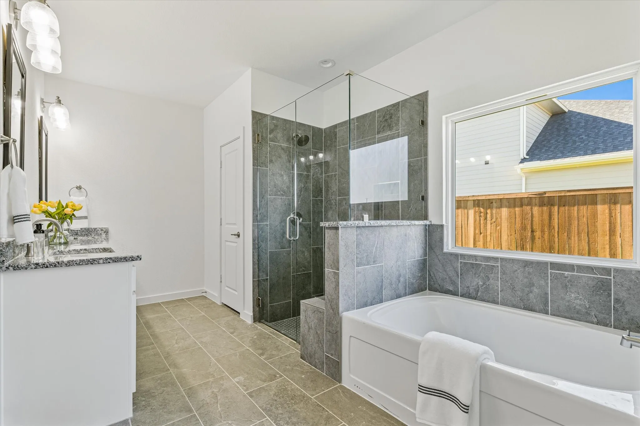 Dual vanity with granite countertops, a walk-in shower with glass enclosure, a built-in soaking tub, and neutral-toned tile flooring