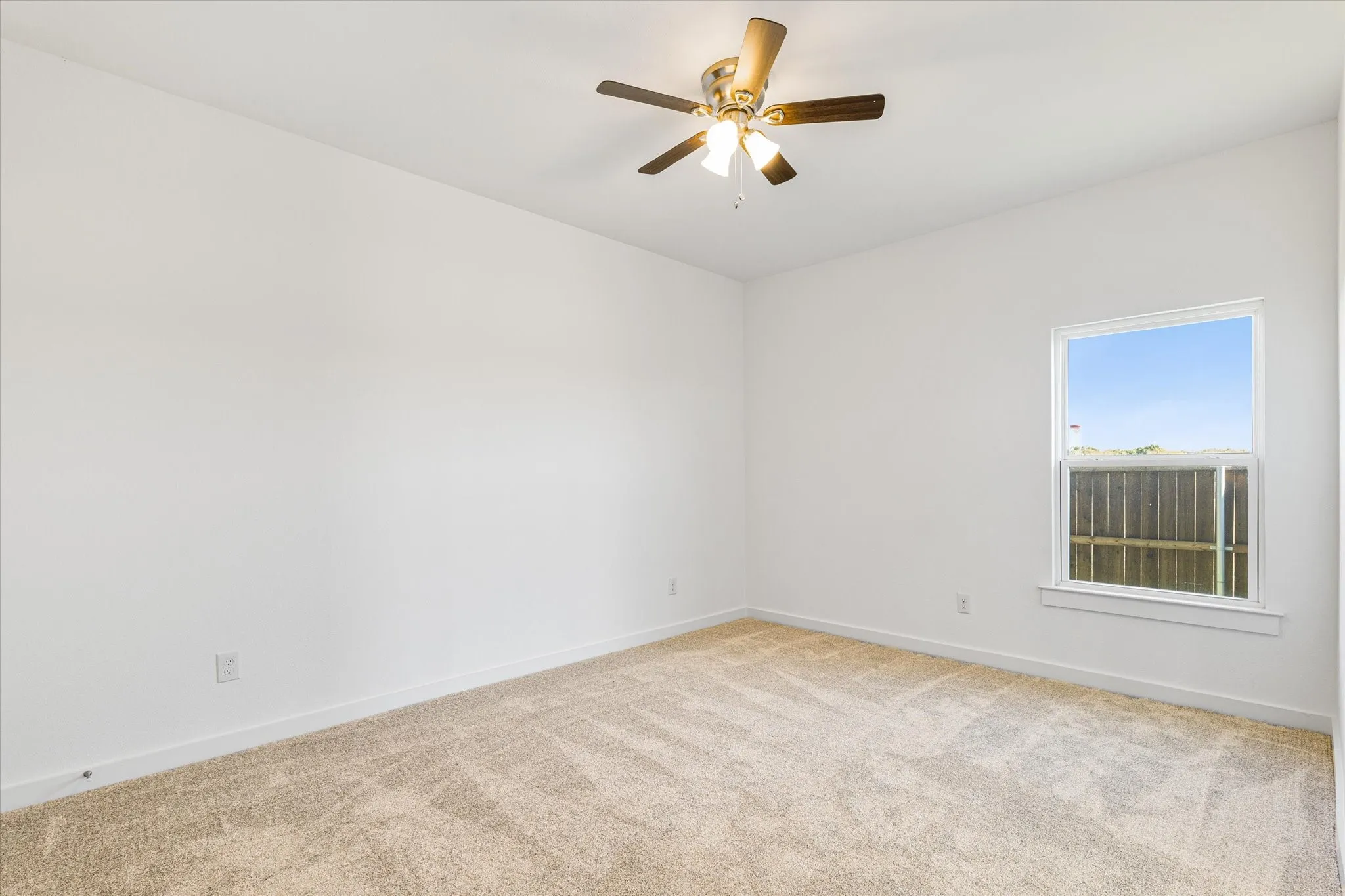 Neutral-toned carpeting, white walls, ceiling-mounted fan with integrated lighting, and a single window with a white frame