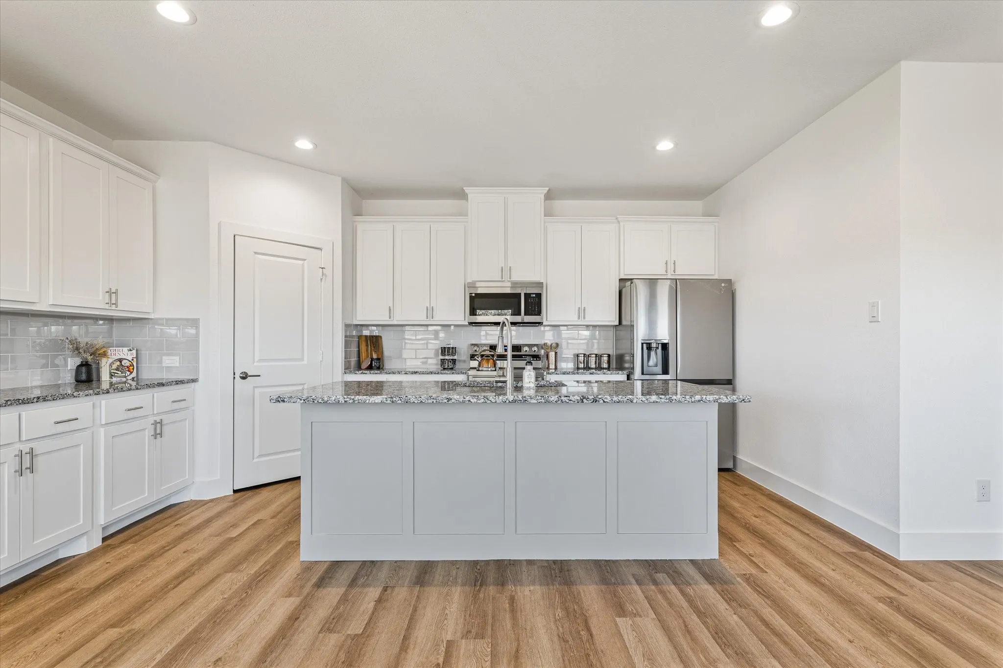 Bright kitchen featuring an expansive center island with stone countertop, wood-finish flooring, white cabinetry, and stainless steel appliances