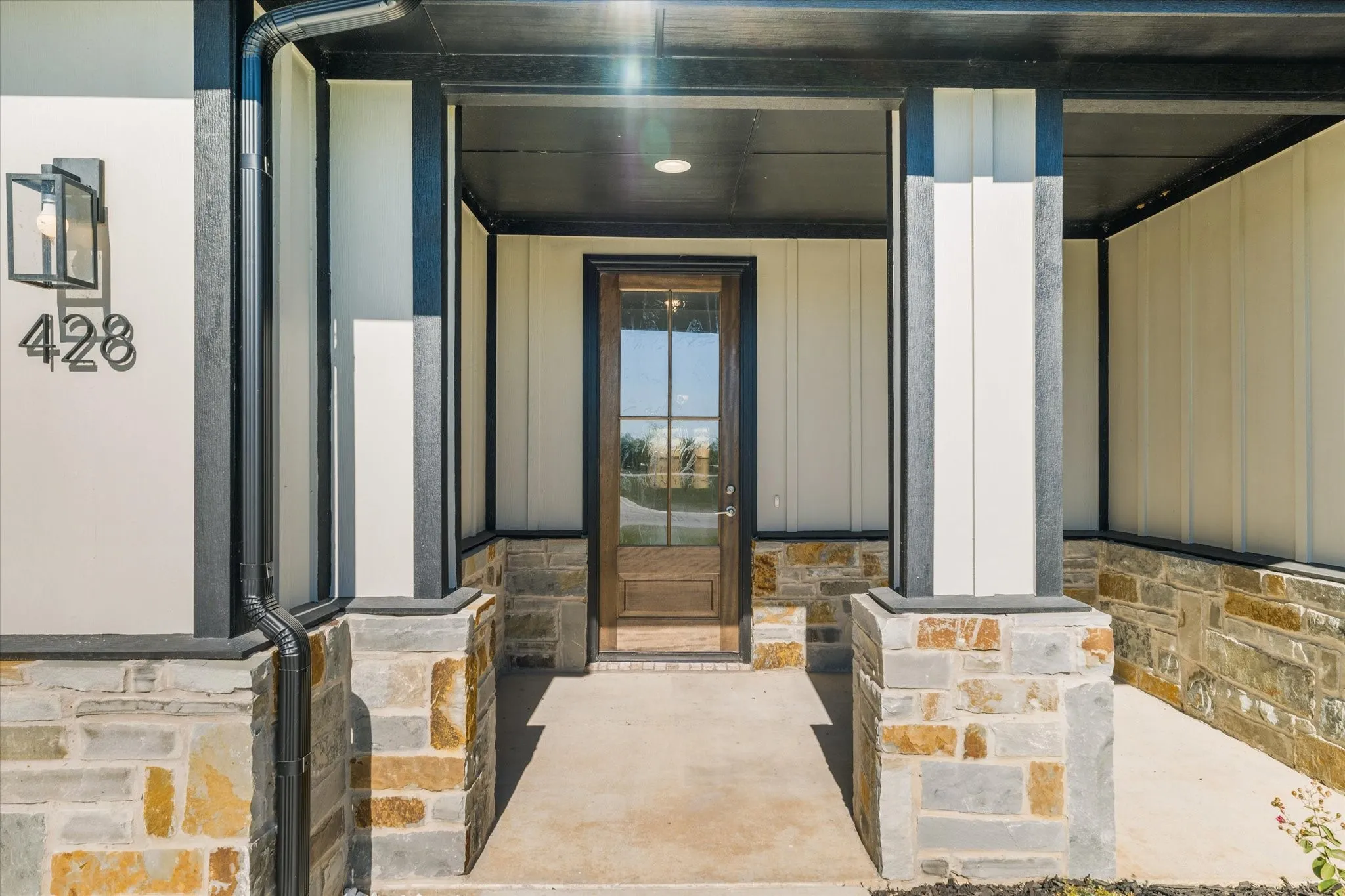 Stone accent facade with board and batten siding, dark wood-finish entry door with glass panels, and a concrete porch