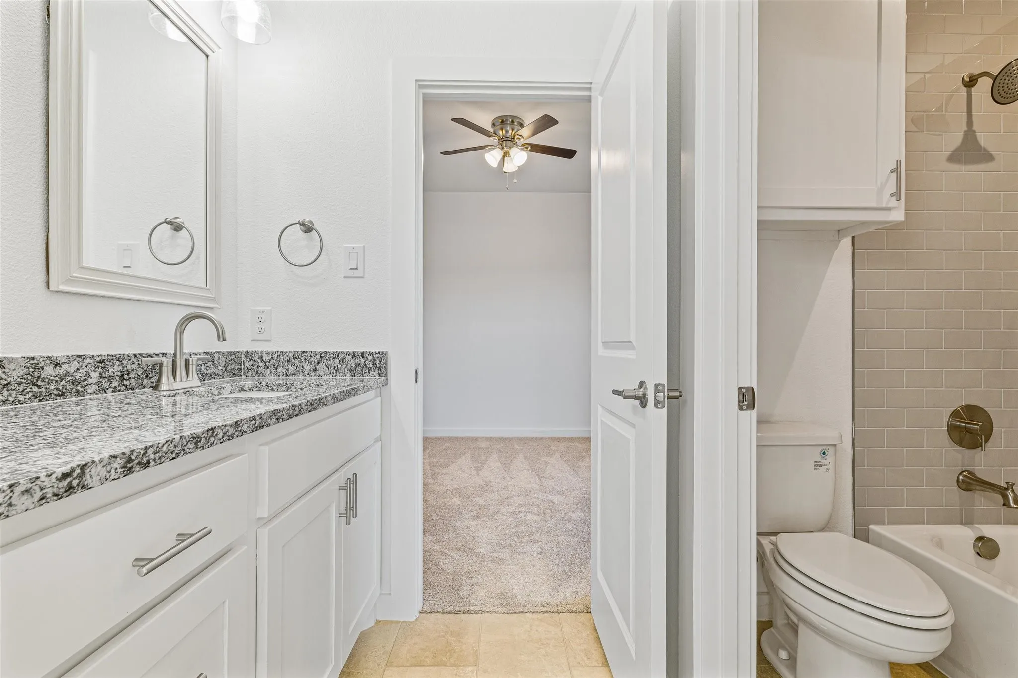 White vanity with a speckled countertop, a rectangular mirror, and brushed nickel fixtures