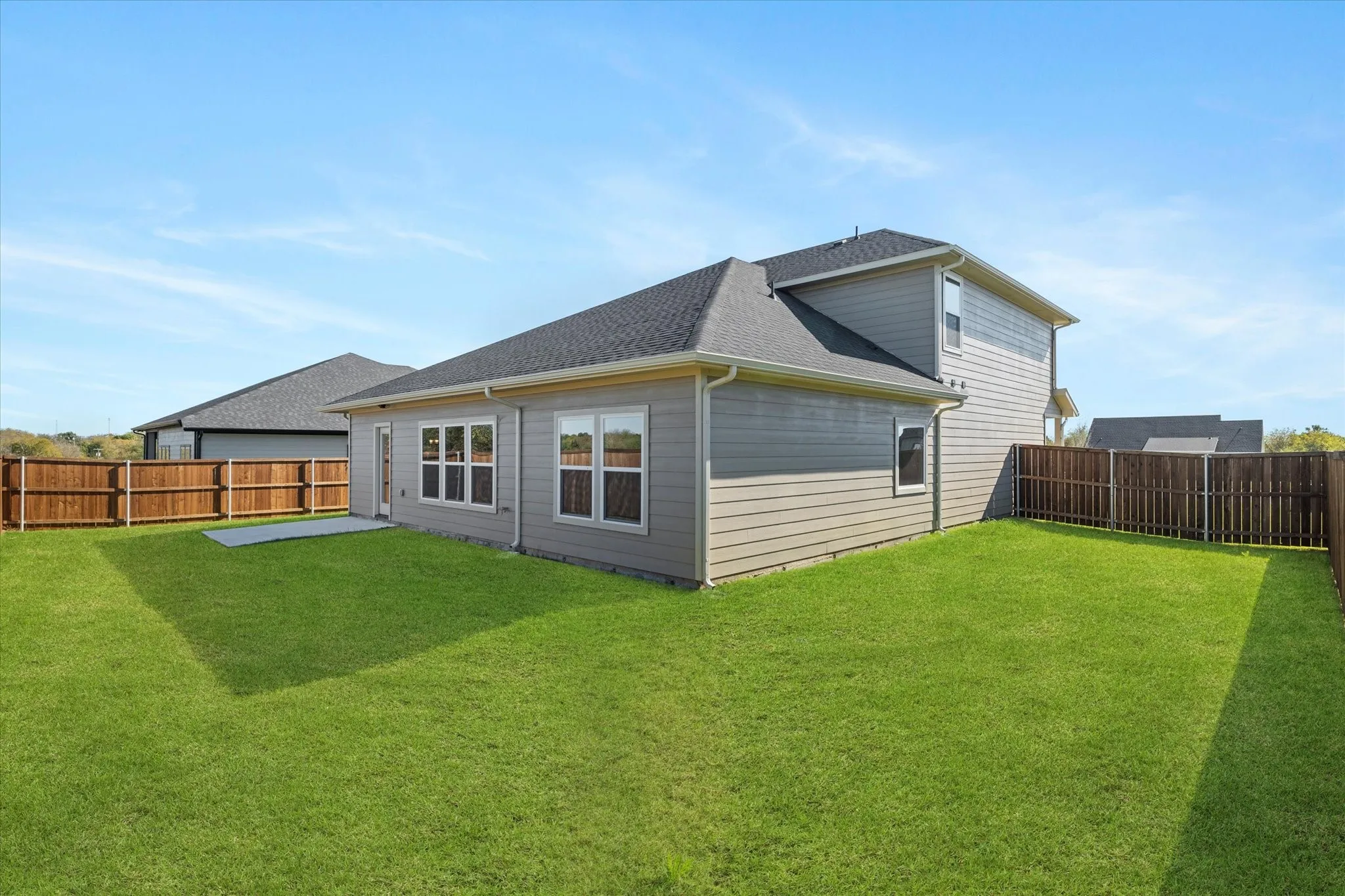 Expansive backyard featuring a manicured lawn, wood privacy fencing, and a concrete patio