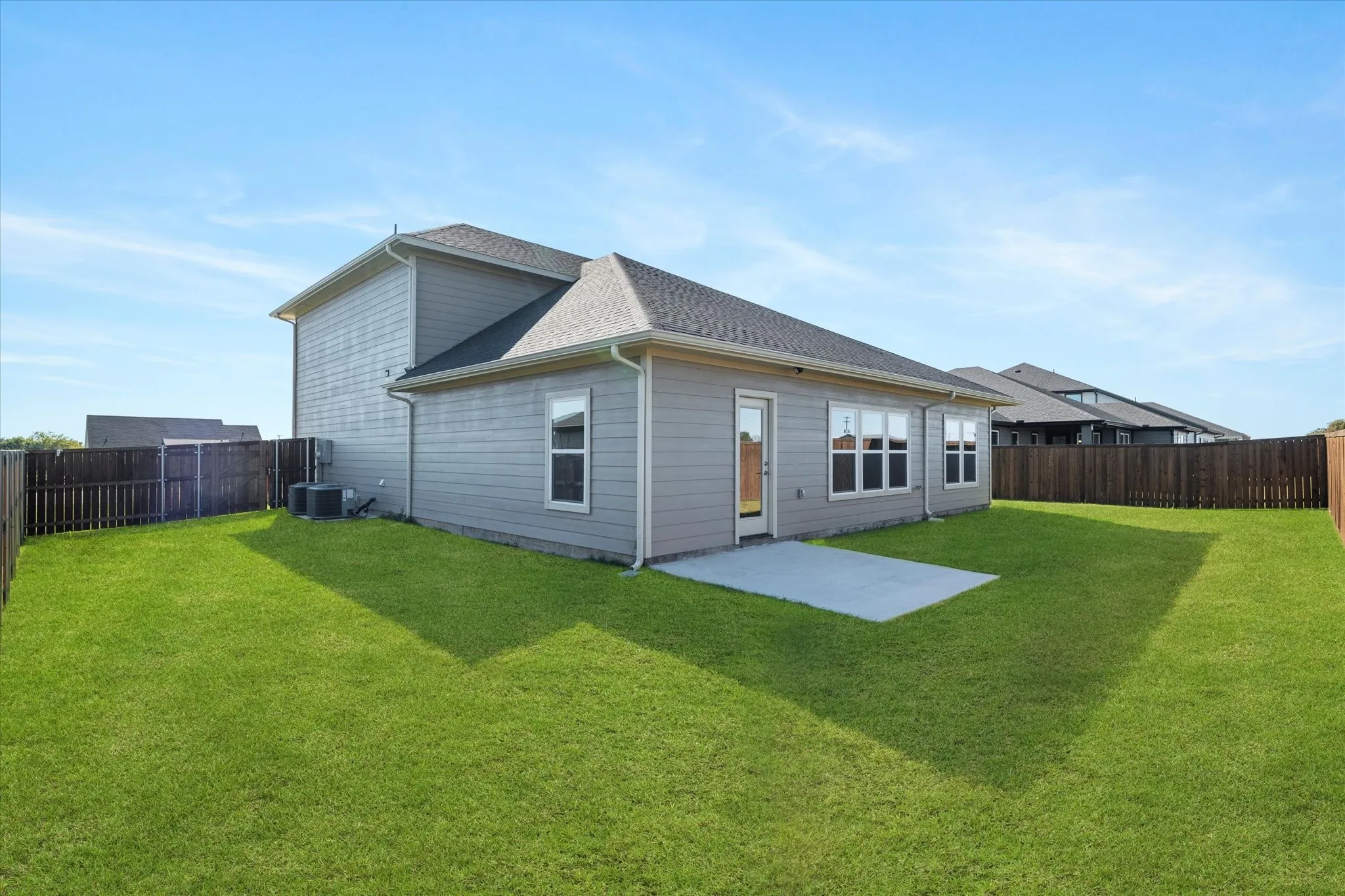 Expansive backyard featuring a manicured lawn, a privacy fence, a concrete patio, and a two-story exterior with siding