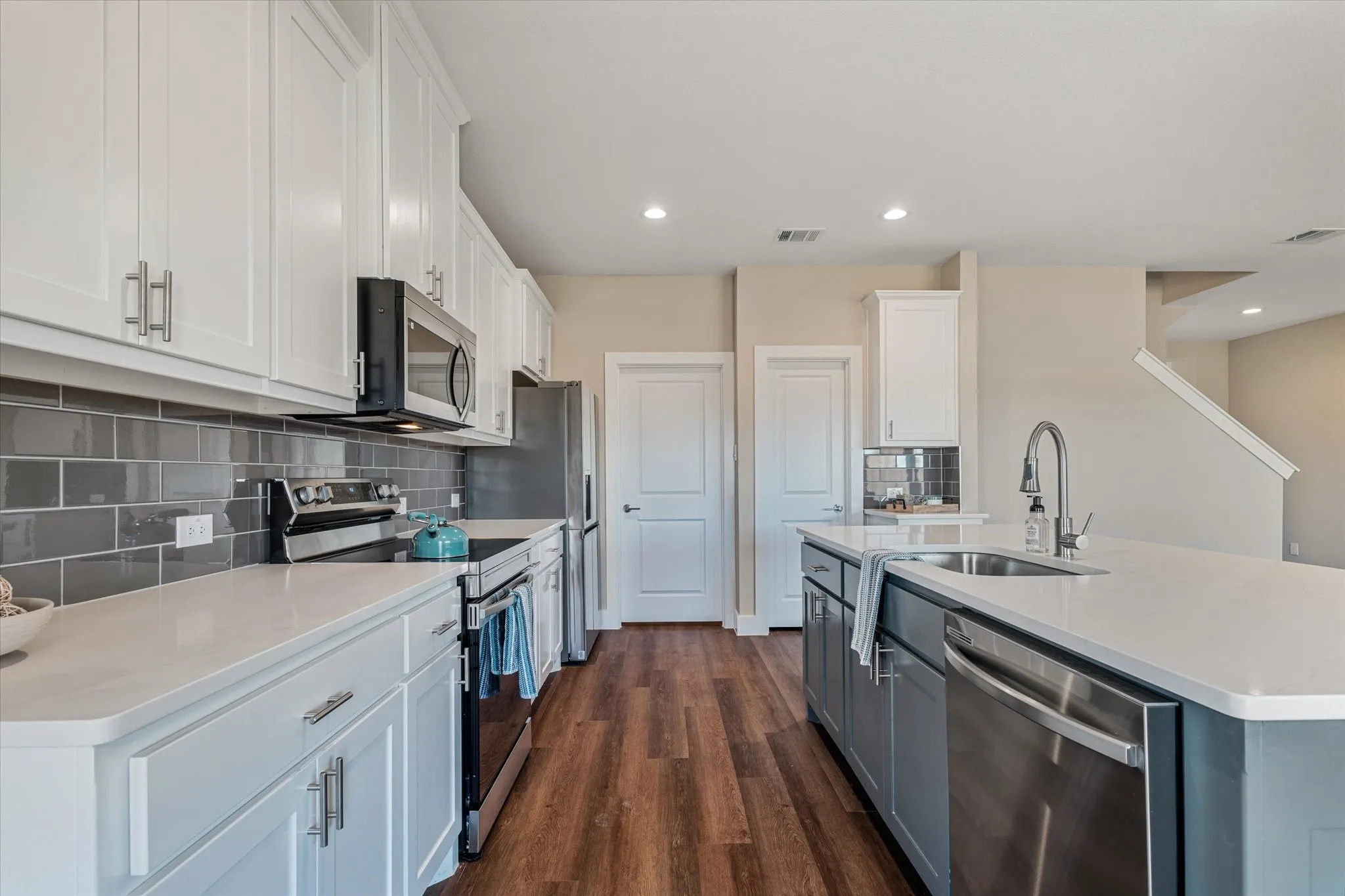 White shaker cabinetry, stainless steel appliances, solid surface countertops, gray subway tile backsplash, and wood-finish flooring