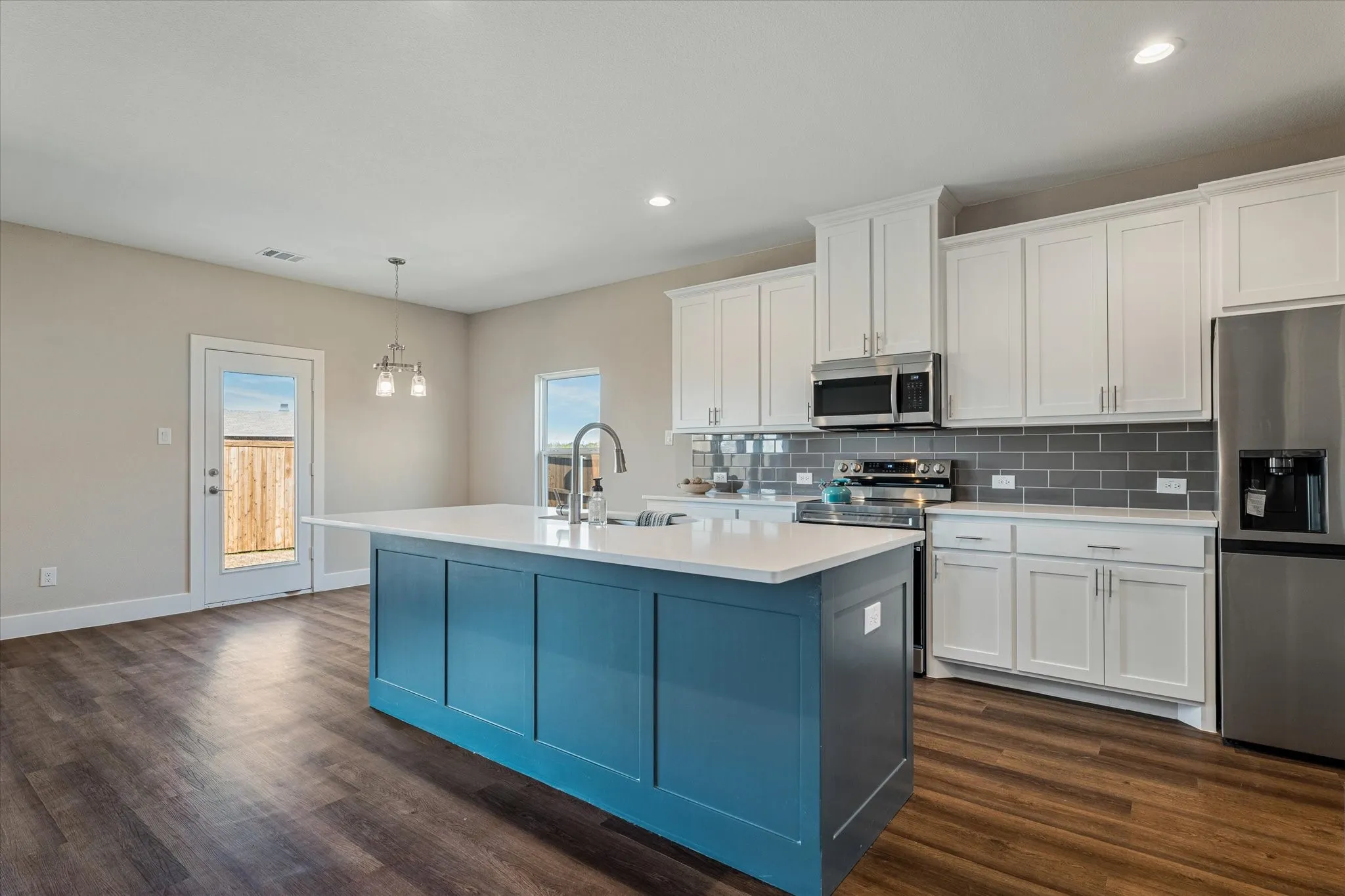Kitchen featuring a central island with white countertop, white upper and lower cabinetry, stainless steel appliances, and a gray subway tile backsplash
